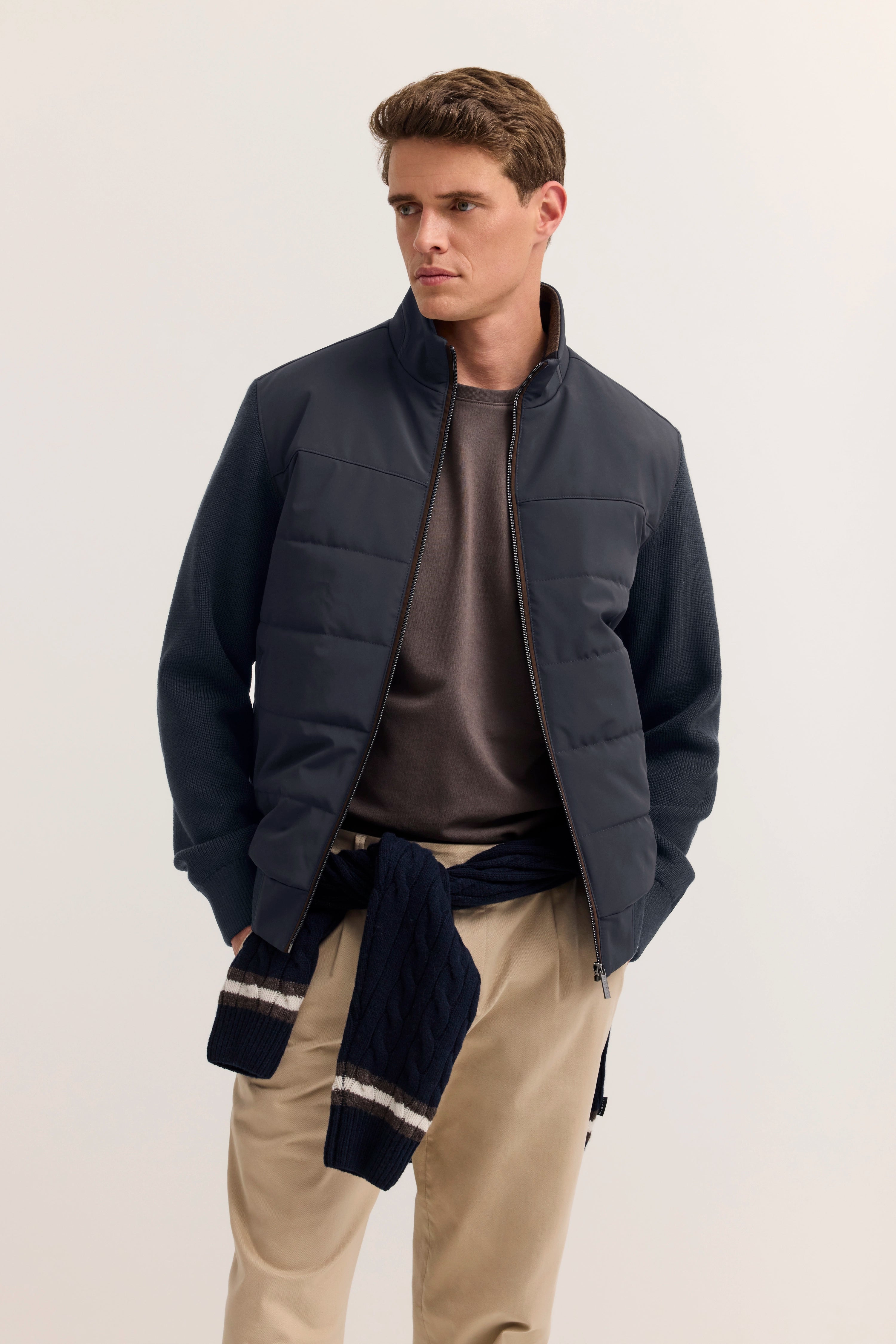 Model trägt bugatti-Outfit: navy Jacke, braunes Shirt, beige Hose, navy Pullover umgebunden.