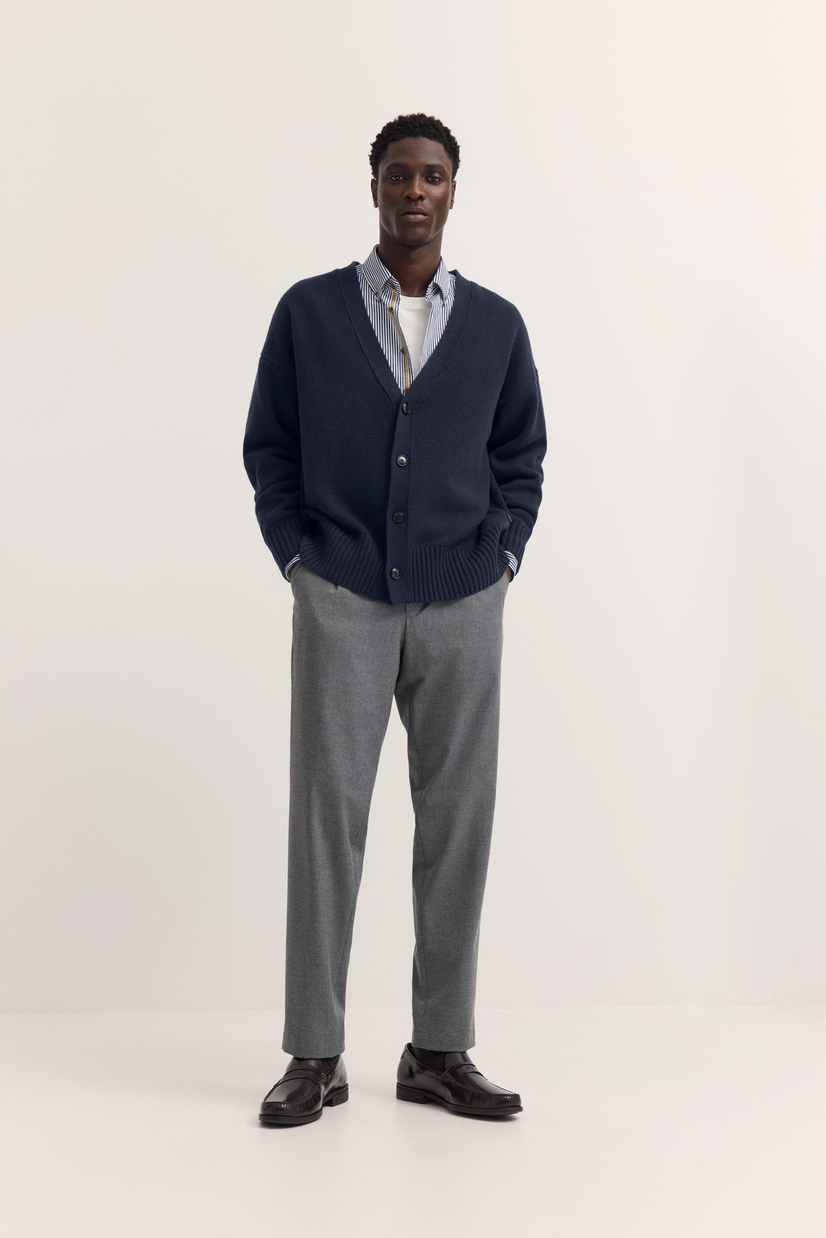 Model in grauem Cardigan und Hemd, graue Hose, schwarze Schuhe, legeres Standing.