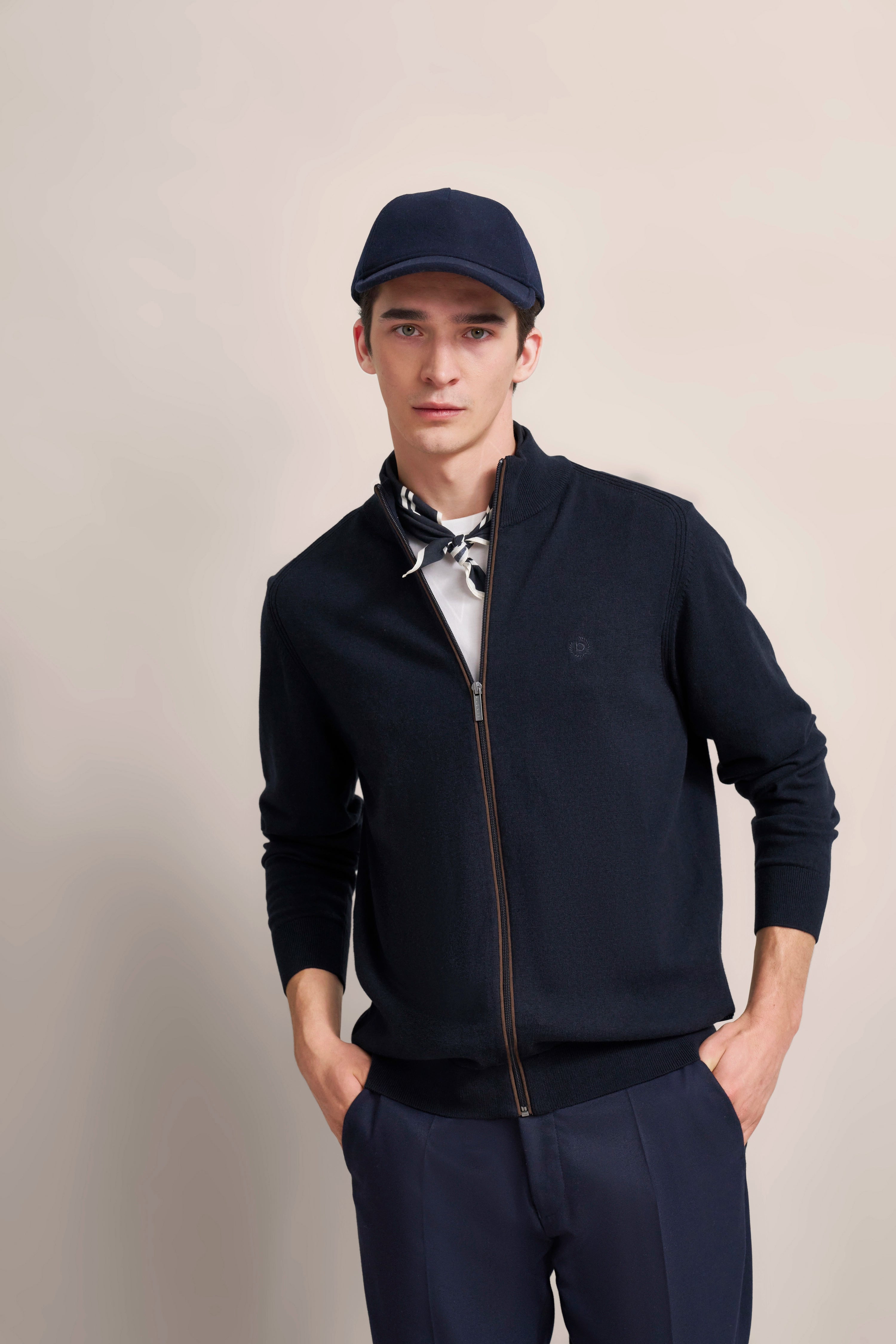 Navy Jacke und Mütze mit weißem Hemd, Model posiert lässig, Hände in Hosentaschen.