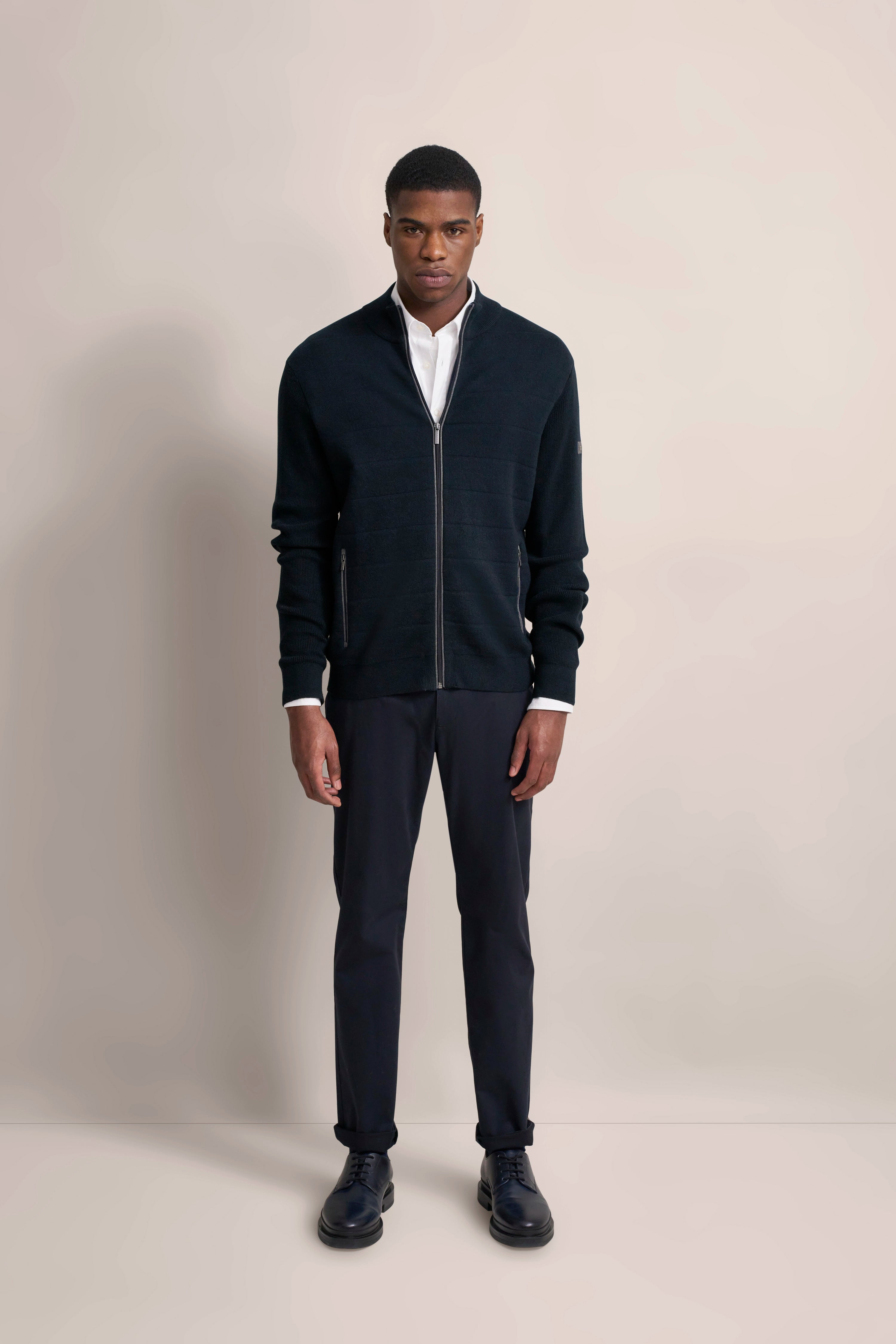 Model in schwarzem bugatti-Cardigan und Hose, weißes Hemd, frontal stehend.