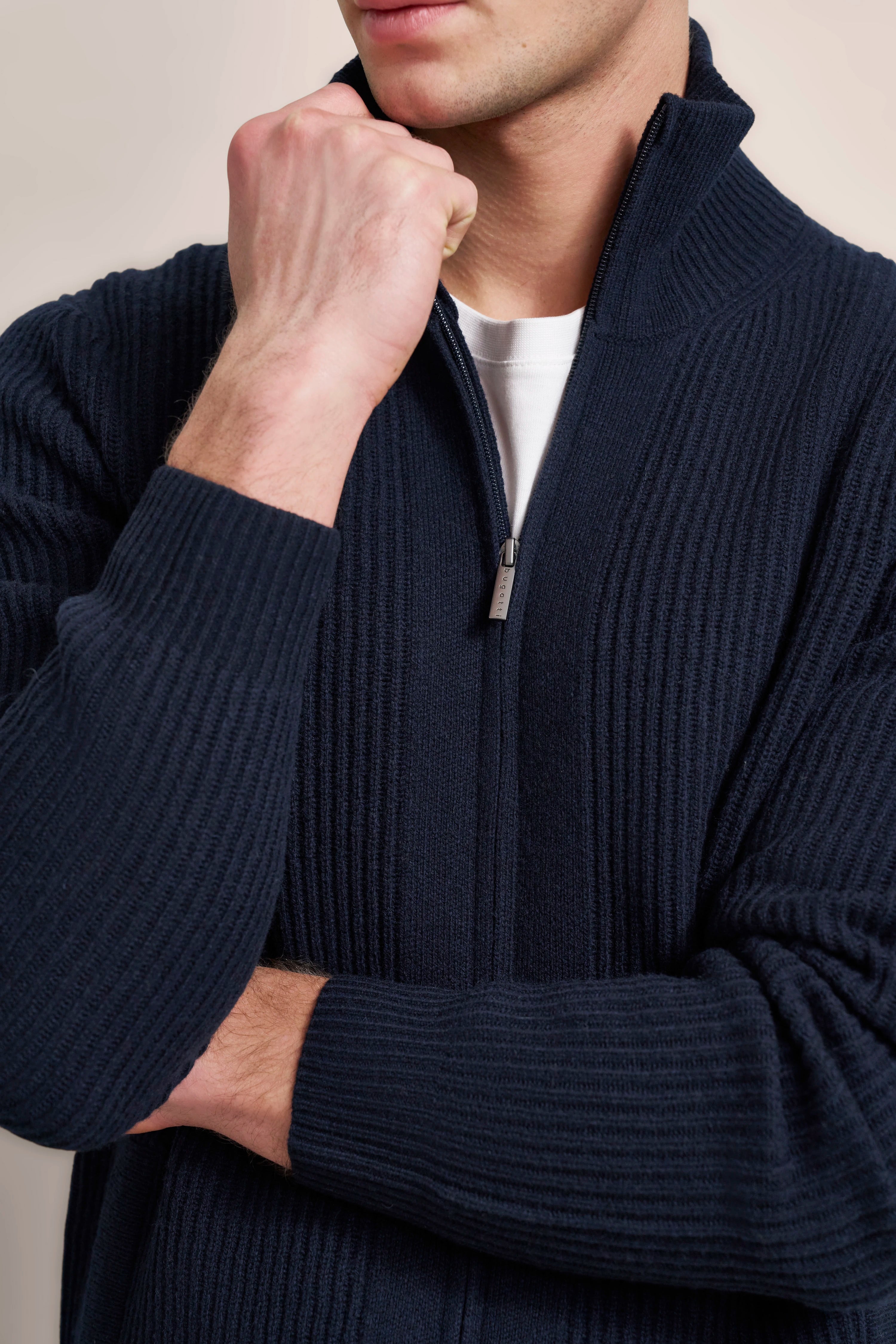 Dunkelblauer bugatti Strickjacke, Modelbild, entspanntes Posing mit erhobenem Arm, weißes Shirt darunter.