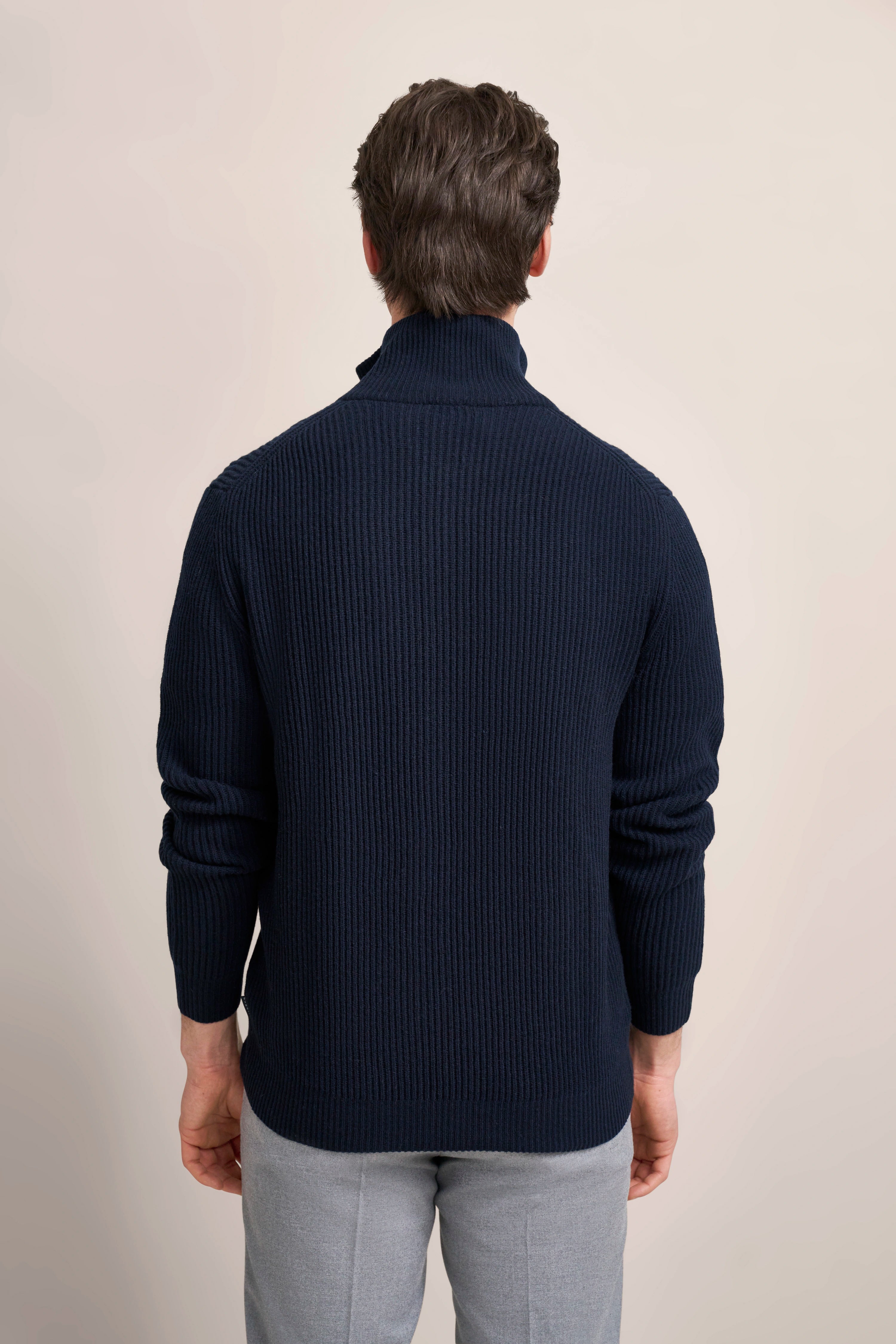 Rückansicht eines Modells in navy bugatti Rollkragenpullover und grauer Hose.