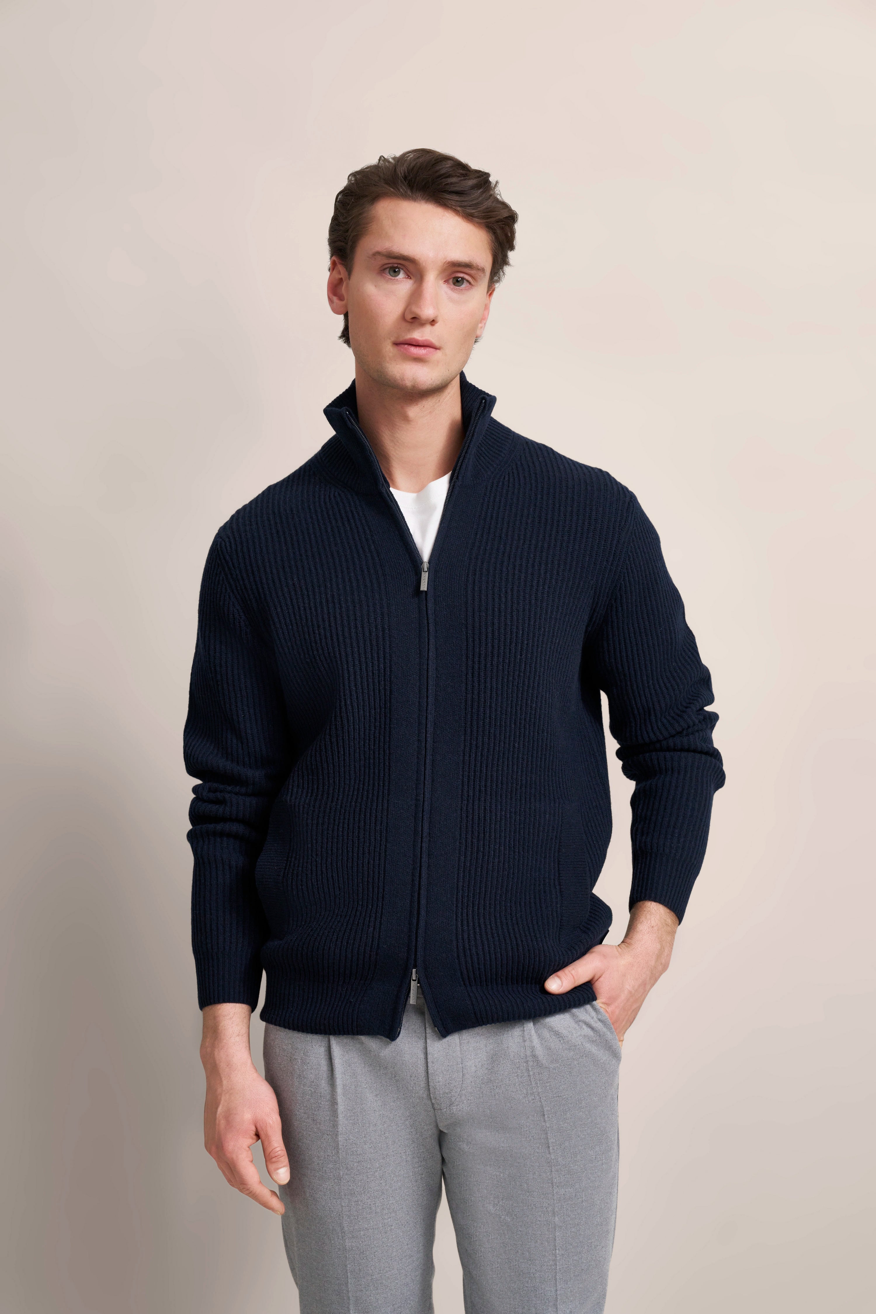 Navy Strickjacke und graue Hose, Model stehend mit Hand in Hosentasche, bugatti Stil und Eleganz.