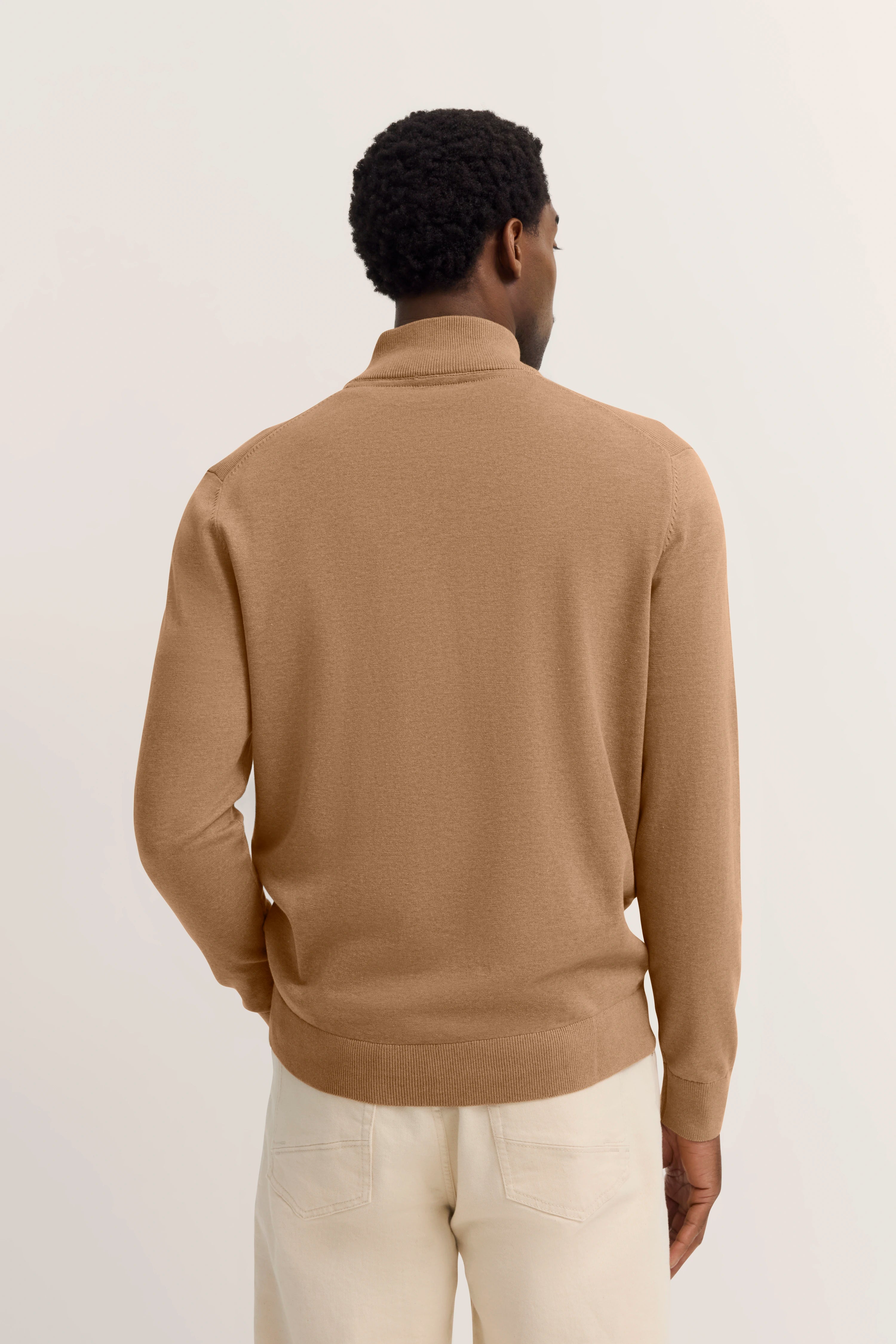Model in beige bugatti-trui, achterkant, casual met crèmekleurige broek.
