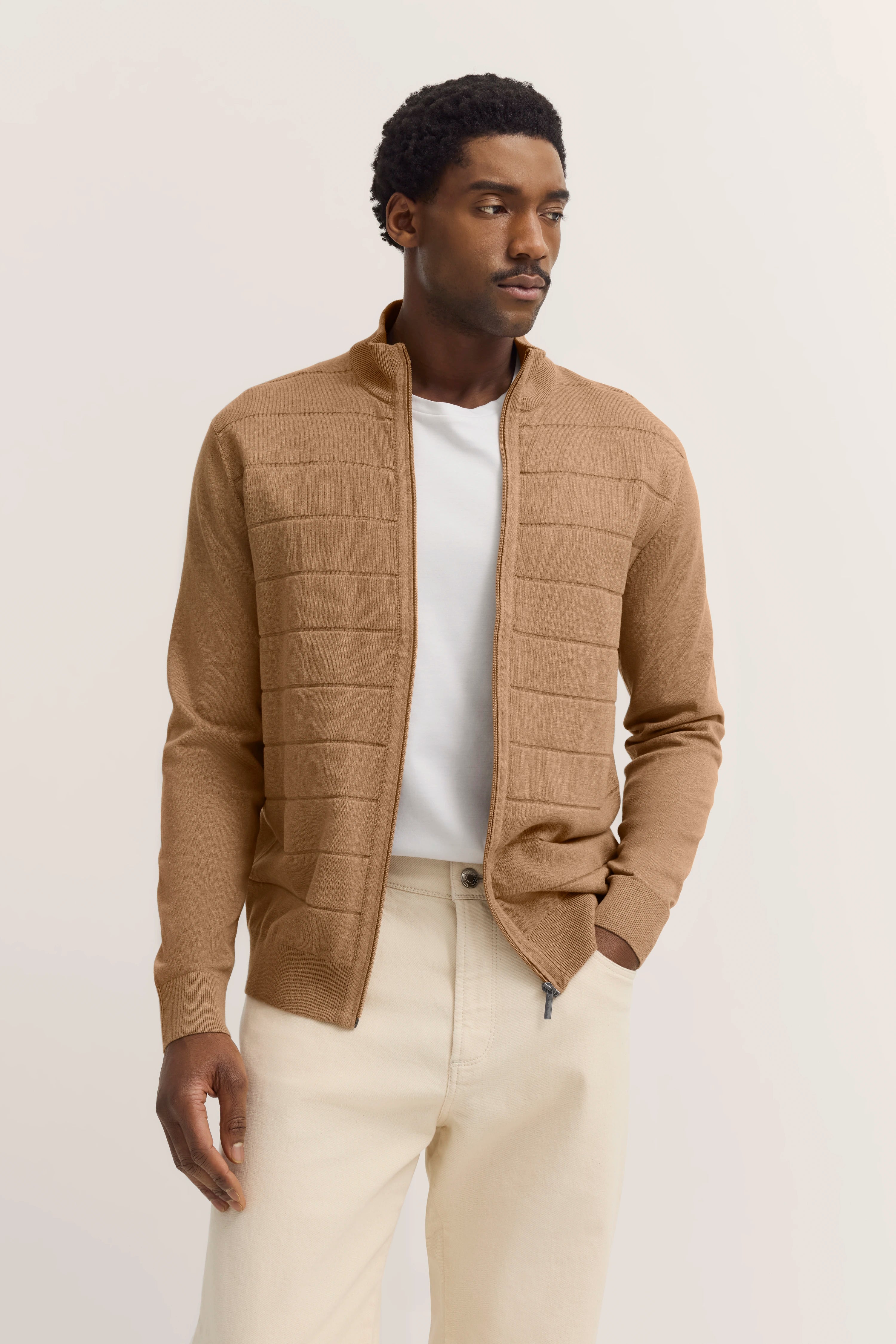 Herenmodel in beige bugatti cardigan, wit shirt en lichte broek, casual pose.