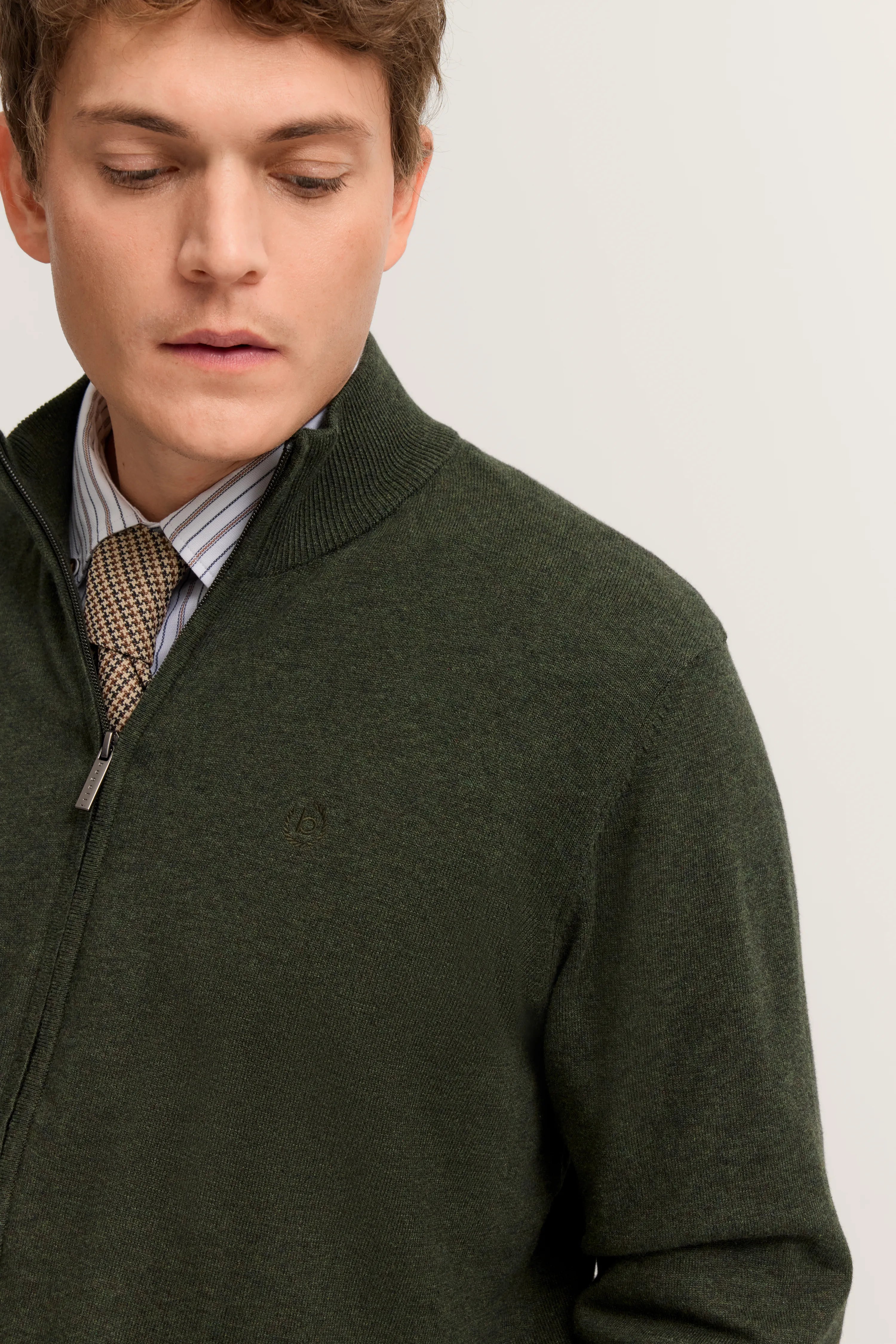 Grüner bugatti Pullover mit Reißverschluss, über gestreiftem Hemd und karierter Krawatte. Modelbild, entspannter Blick.