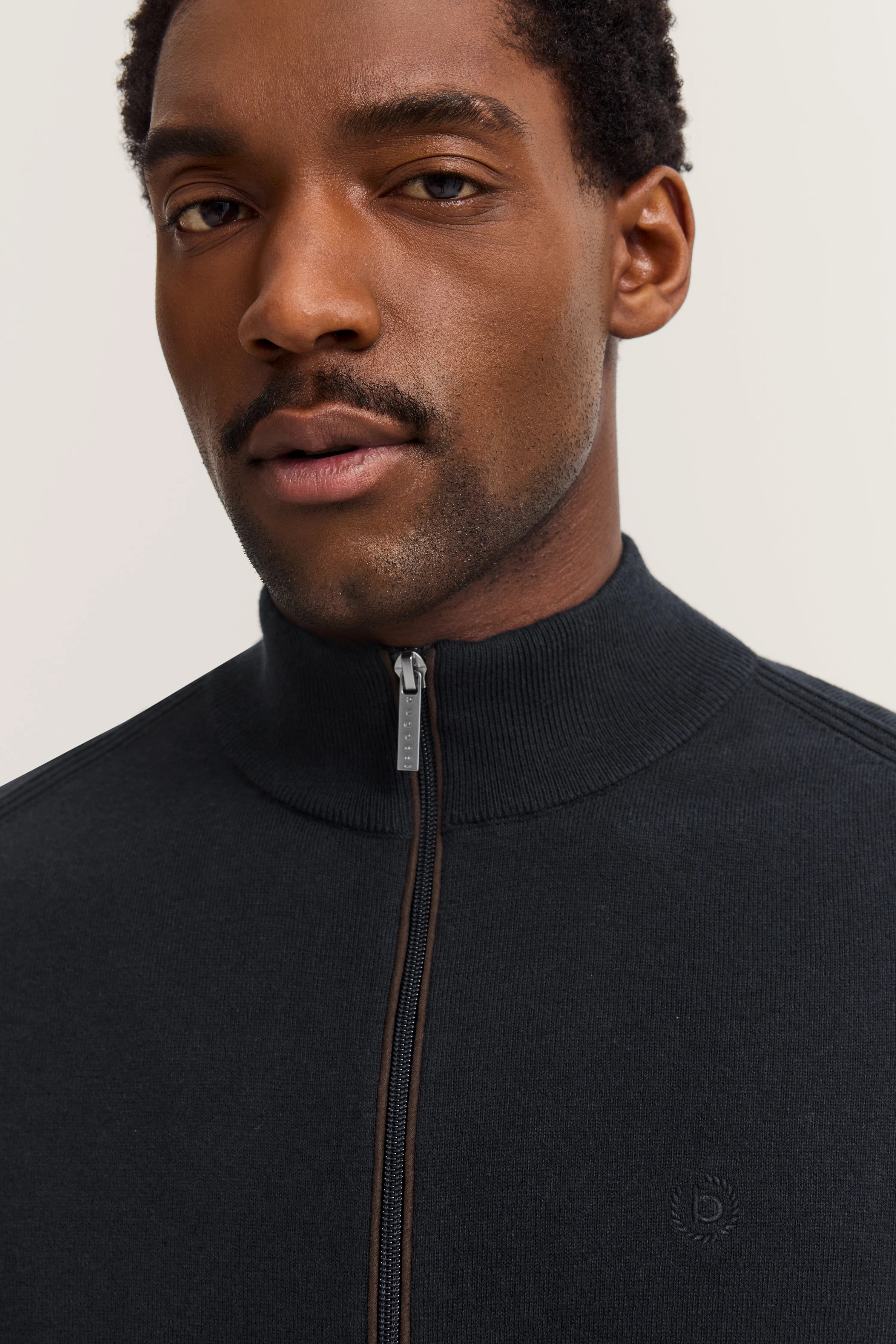 Headshot of a man in a dark blue bugatti zip-up sweater with stand-up collar.