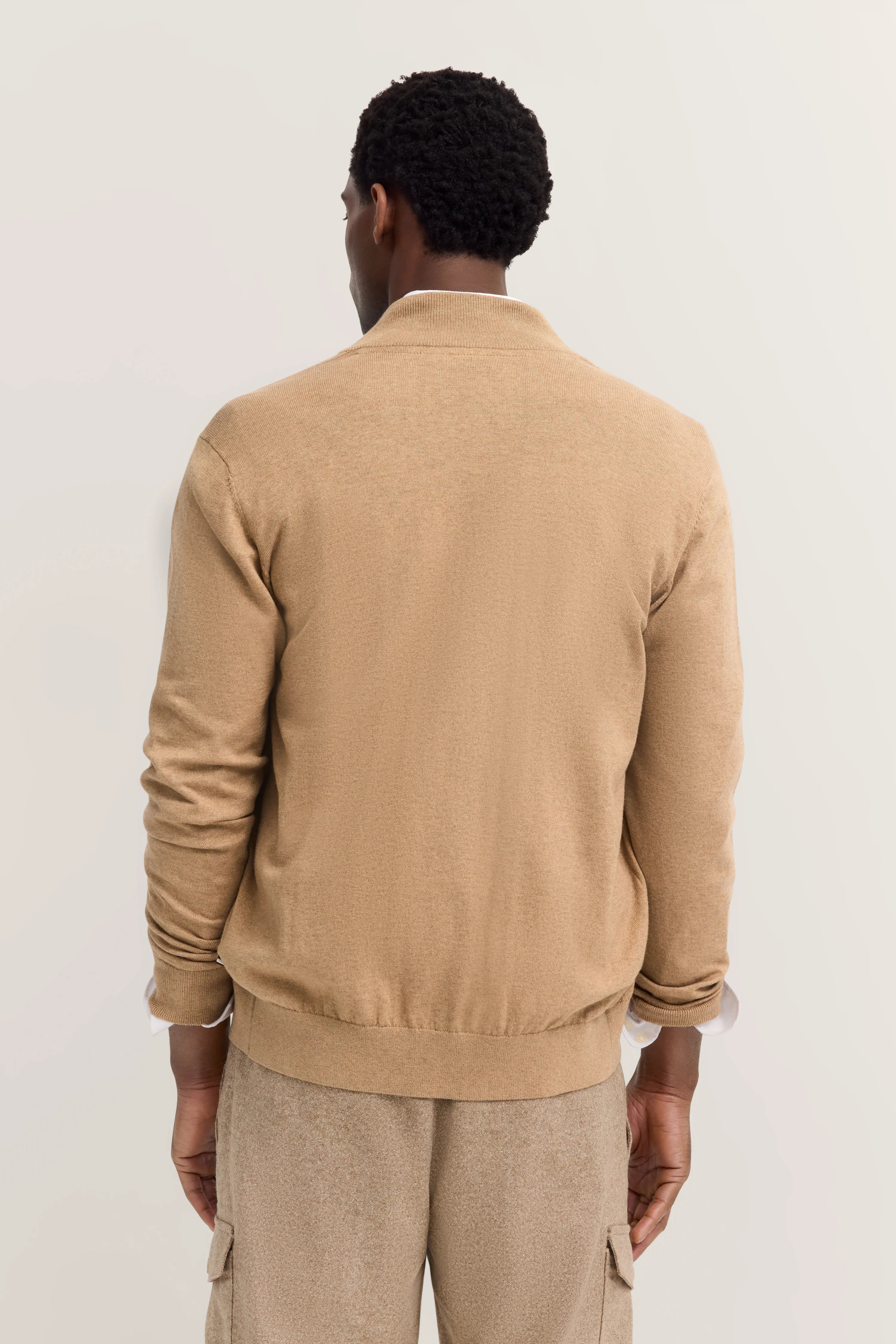bugatti model in beige outfit, achterkant. Casual styling met jas en broek, ontspannen pose.