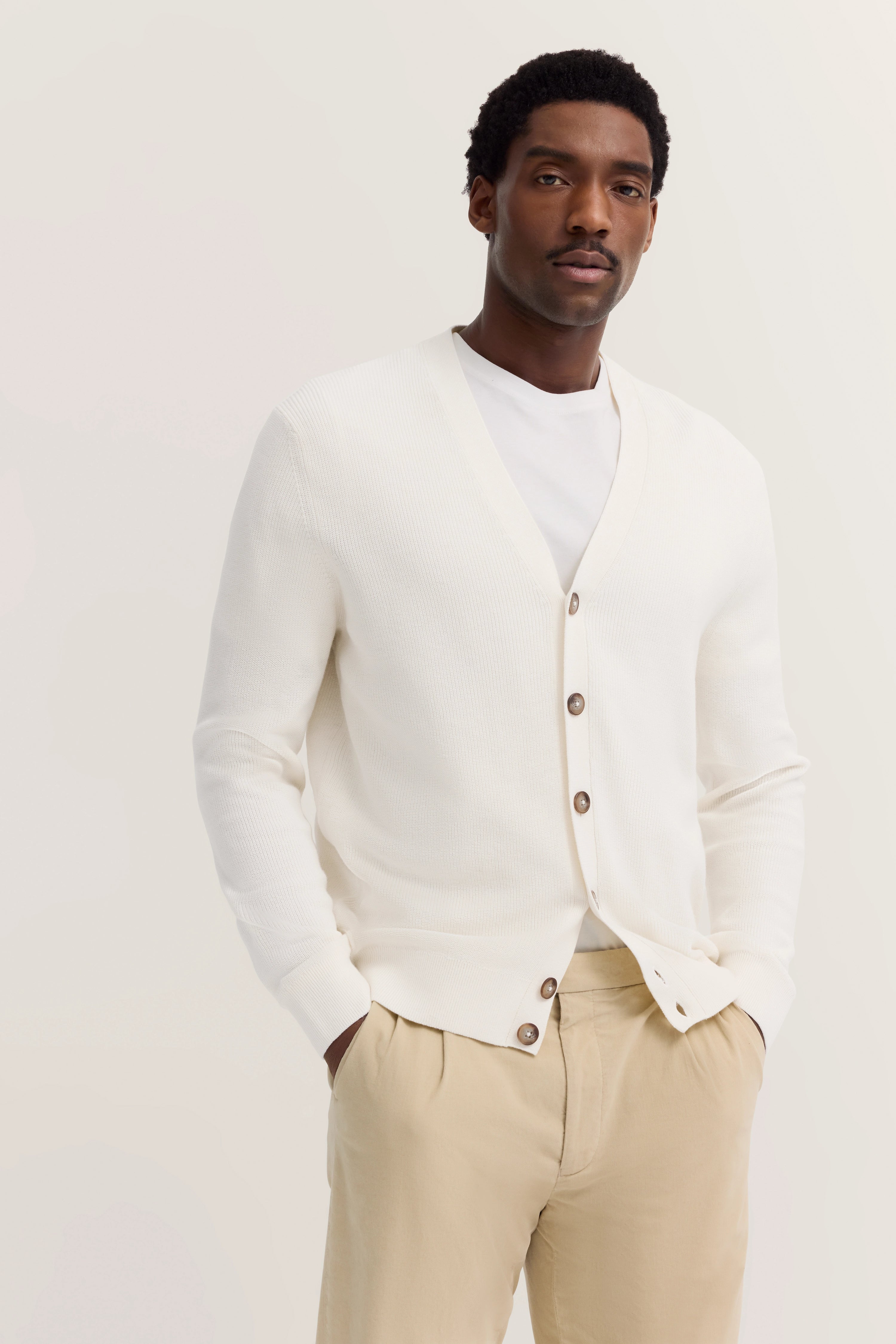 White cardigan, beige trousers, relaxed model, casual pose, inspired by Italy's elegance and bugatti's refined style.