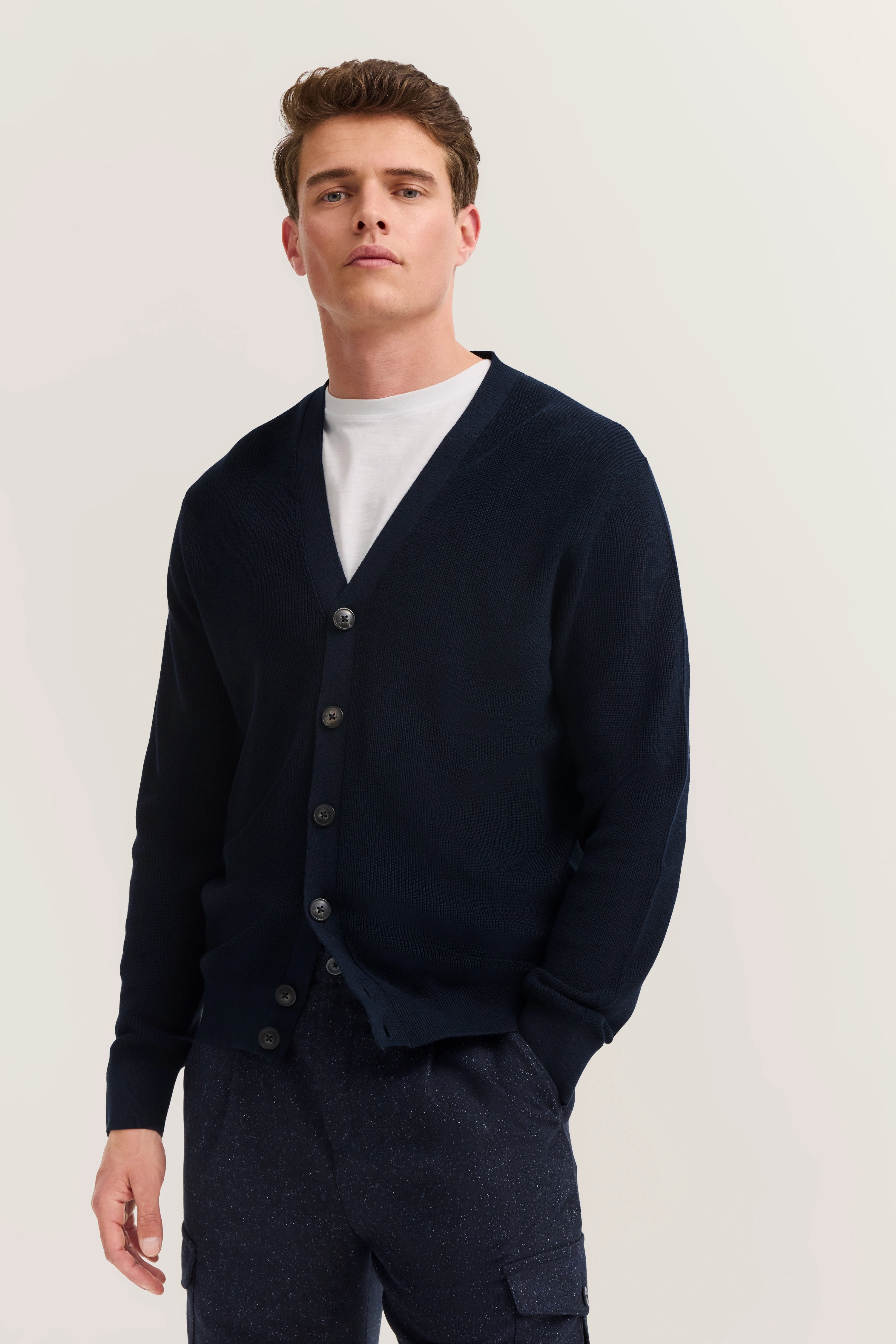 Model in dunkelblauer bugatti Strickjacke, weißem T-Shirt, lässig stehend, entspannter urbaner Stil.