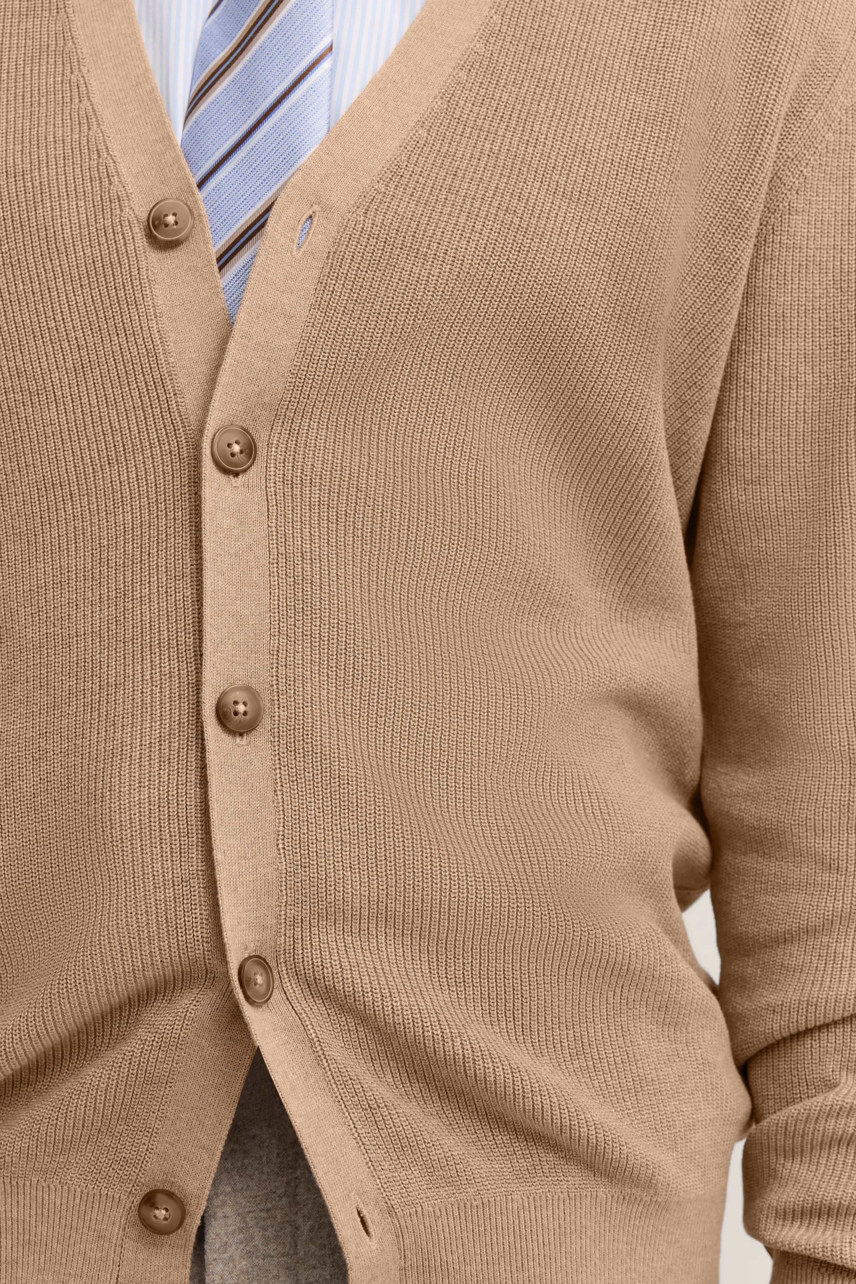 Beige Cardigan mit Knöpfen, über gestreiftem Hemd und Krawatte. Büstenbild.