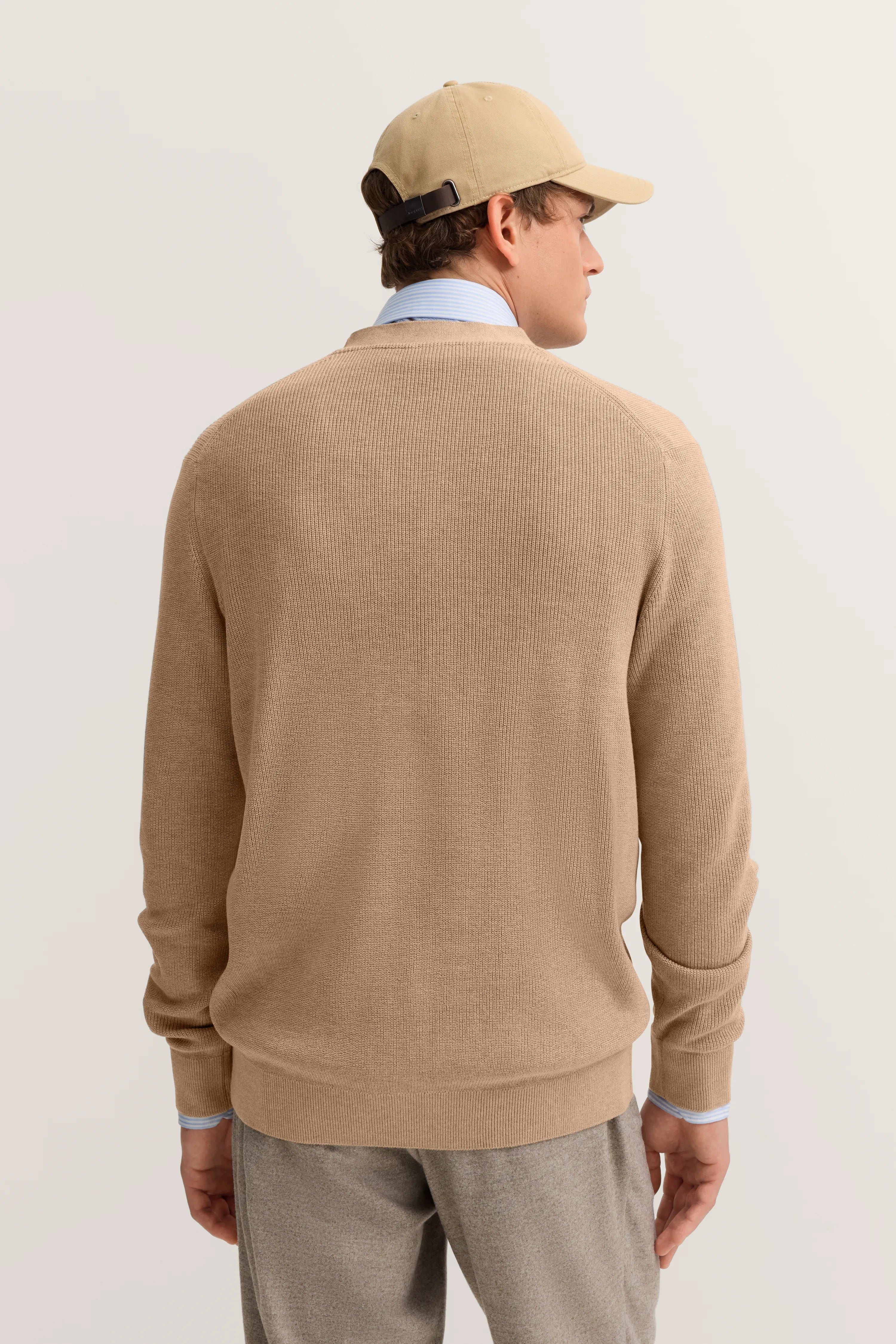 Beiger Pullover und Kappe, hellblaues Hemd, graue Hose, Modelbild von hinten bei bugatti.