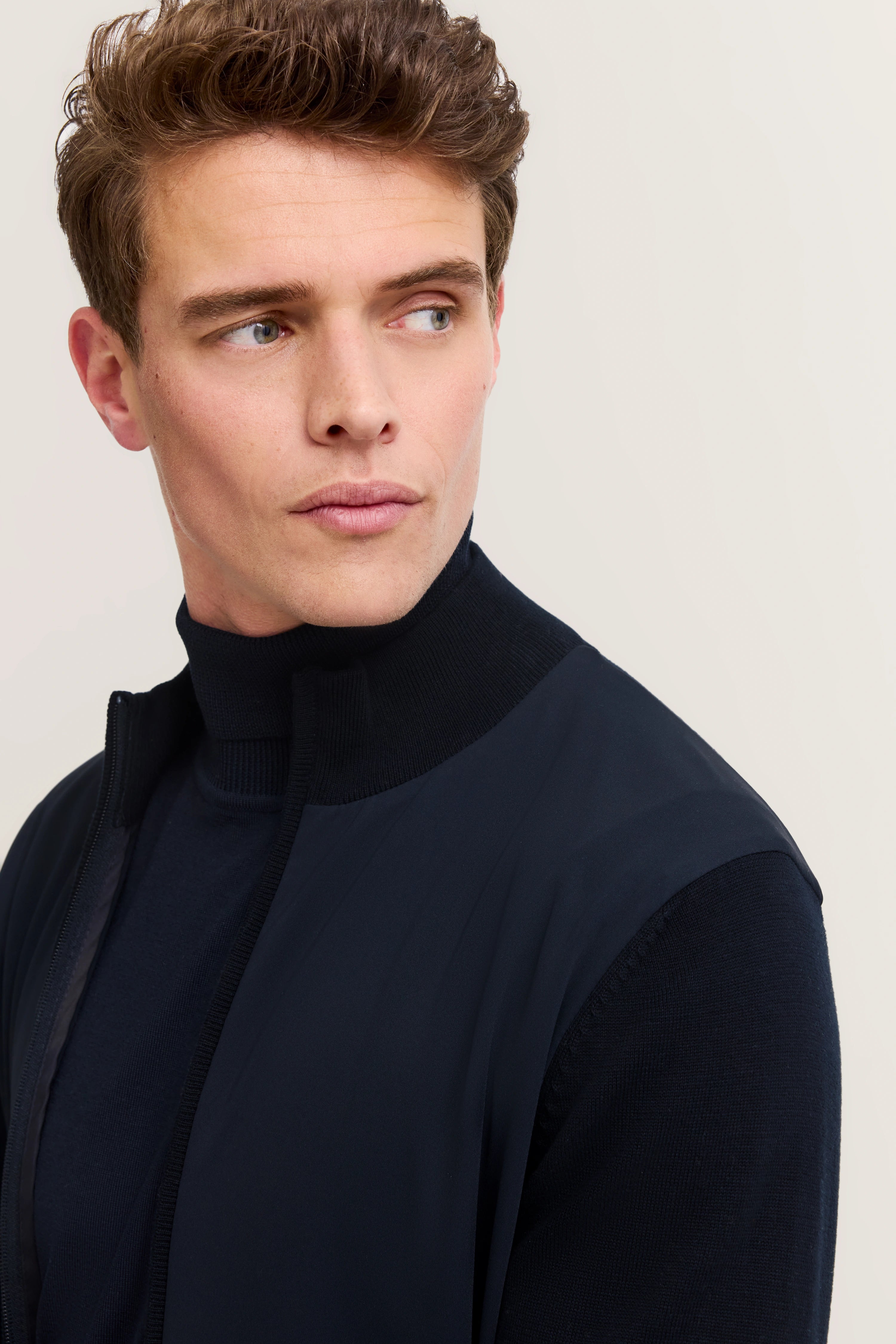 bugatti Modelbild: Mann in navyblauem Stehkragenpullover, leichtes Lächeln, seitlicher Blick.