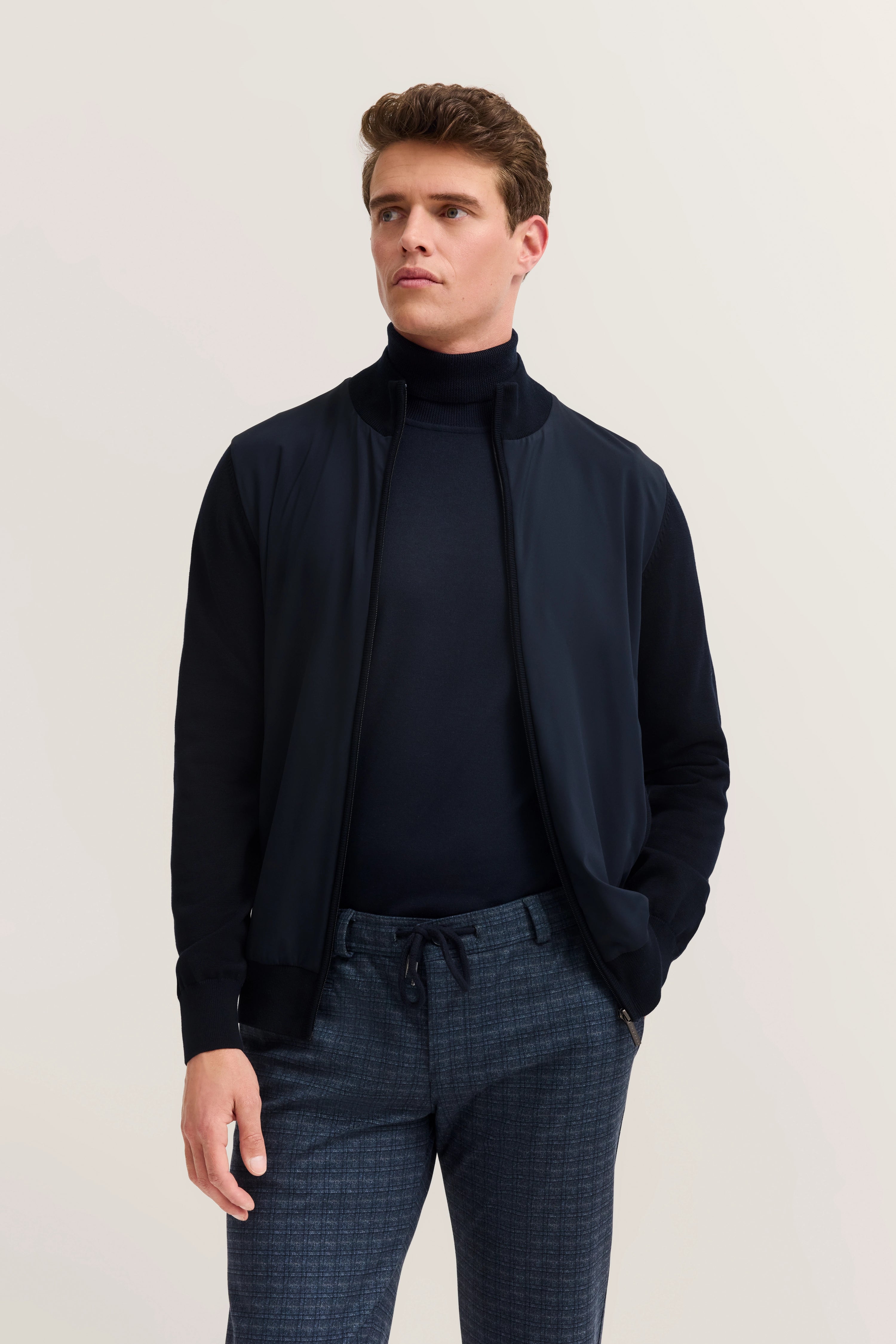 Model in bugatti outfit: Dark jacket, turtleneck, plaid pants, relaxed pose.