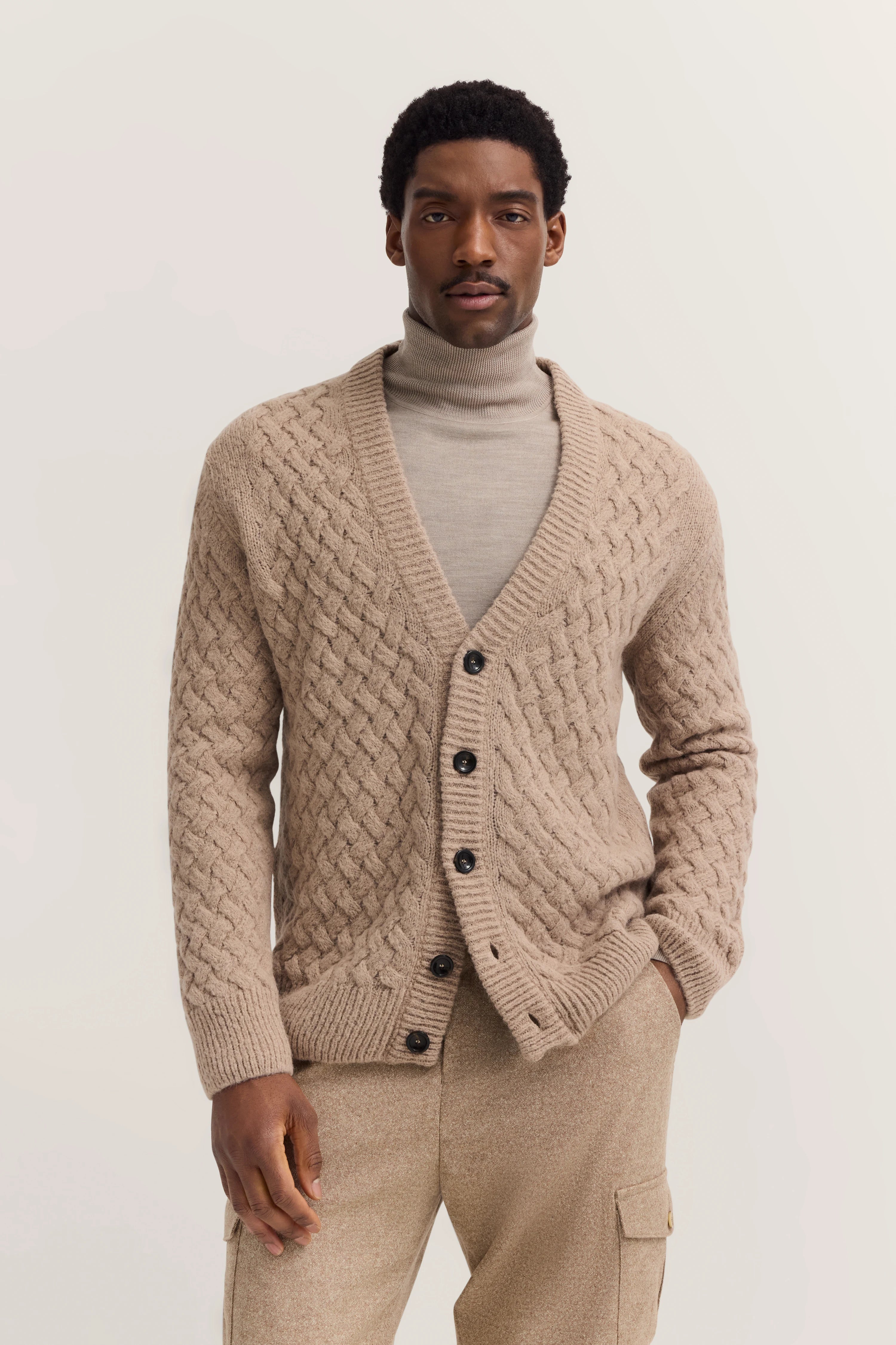 Beiger Cardigan mit Zopfmuster und Rollkragenpullover, Modelbild mit entspanntem Posing.