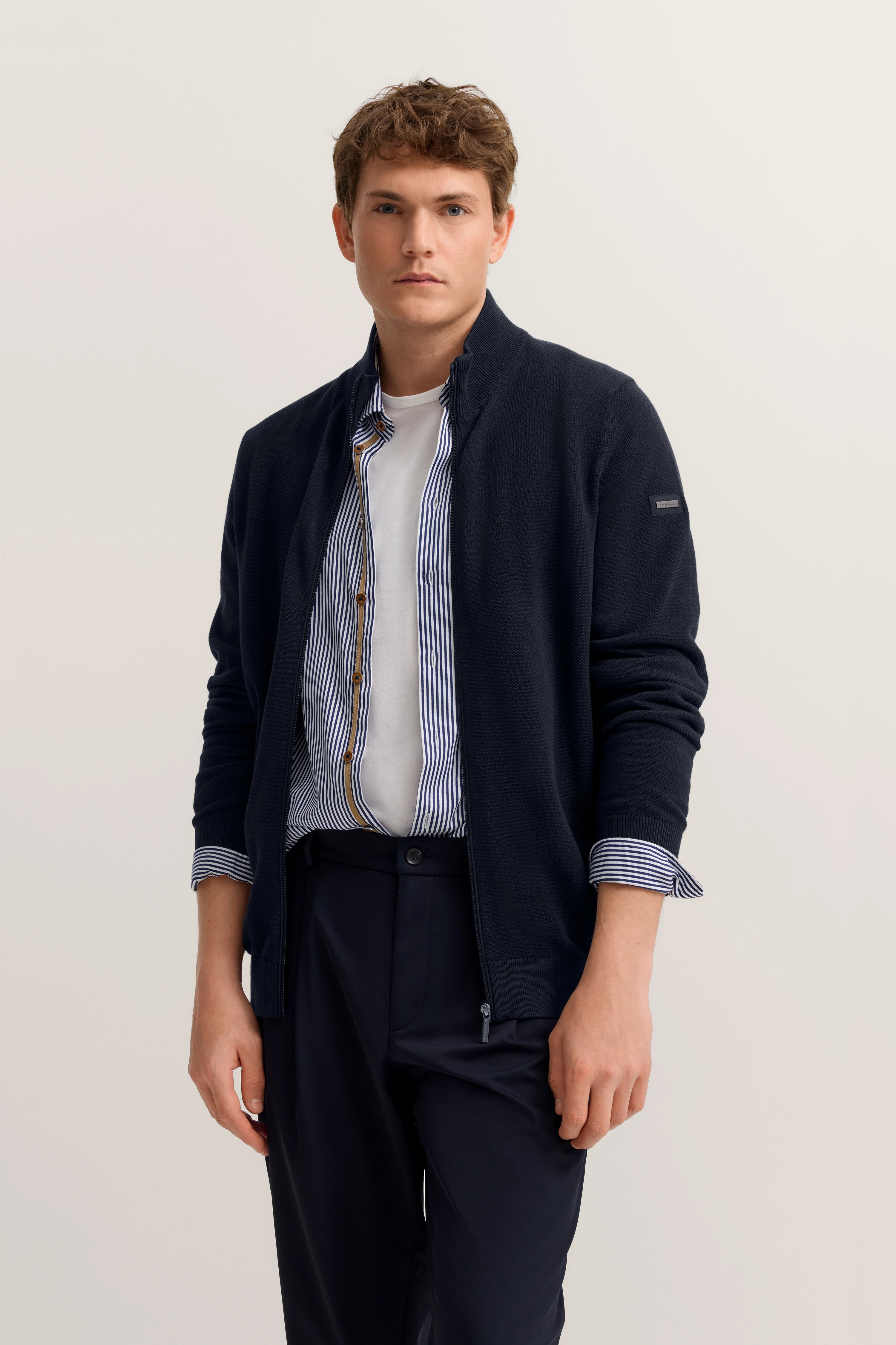 Model trägt bugatti-Outfit: navy Jacke, gestreiftes Hemd, weiße T-Shirt, dunkle Hose