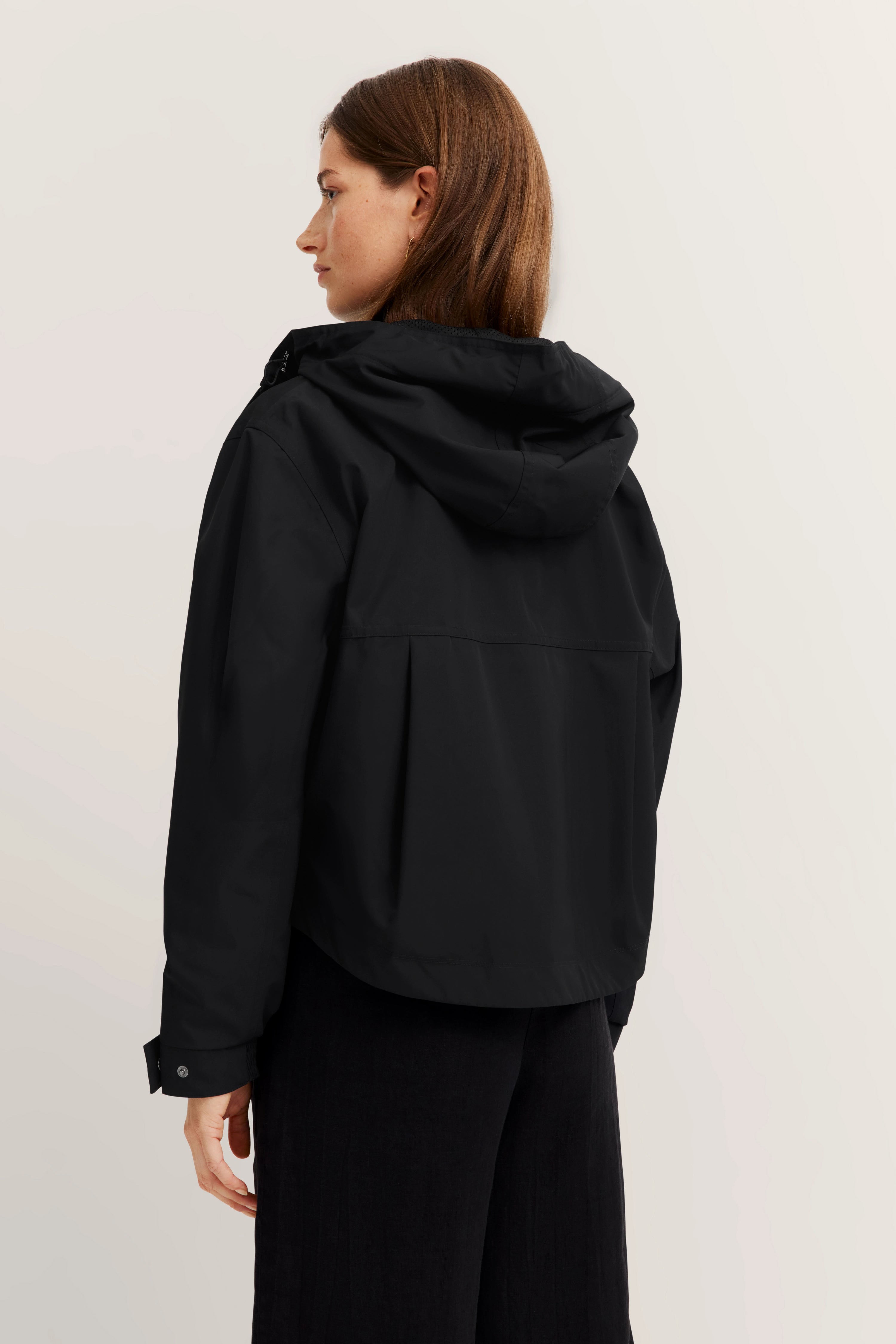 Schwarze bugatti Jacke mit Kapuze, Model von hinten, legeres Posing.