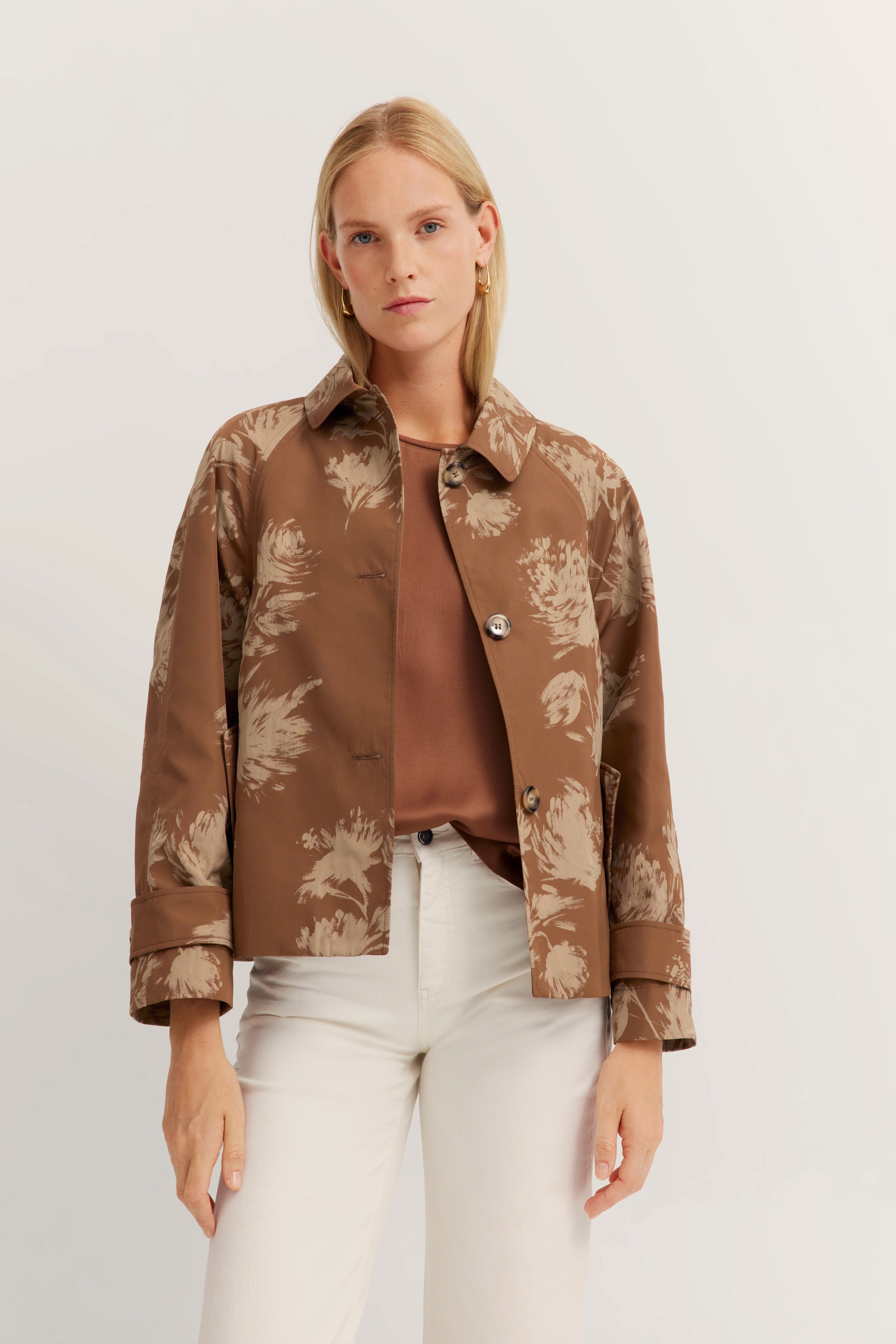 Braune gemusterte Jacke, braunes Shirt, weiße Hose, Model stehend, bugatti Stil.