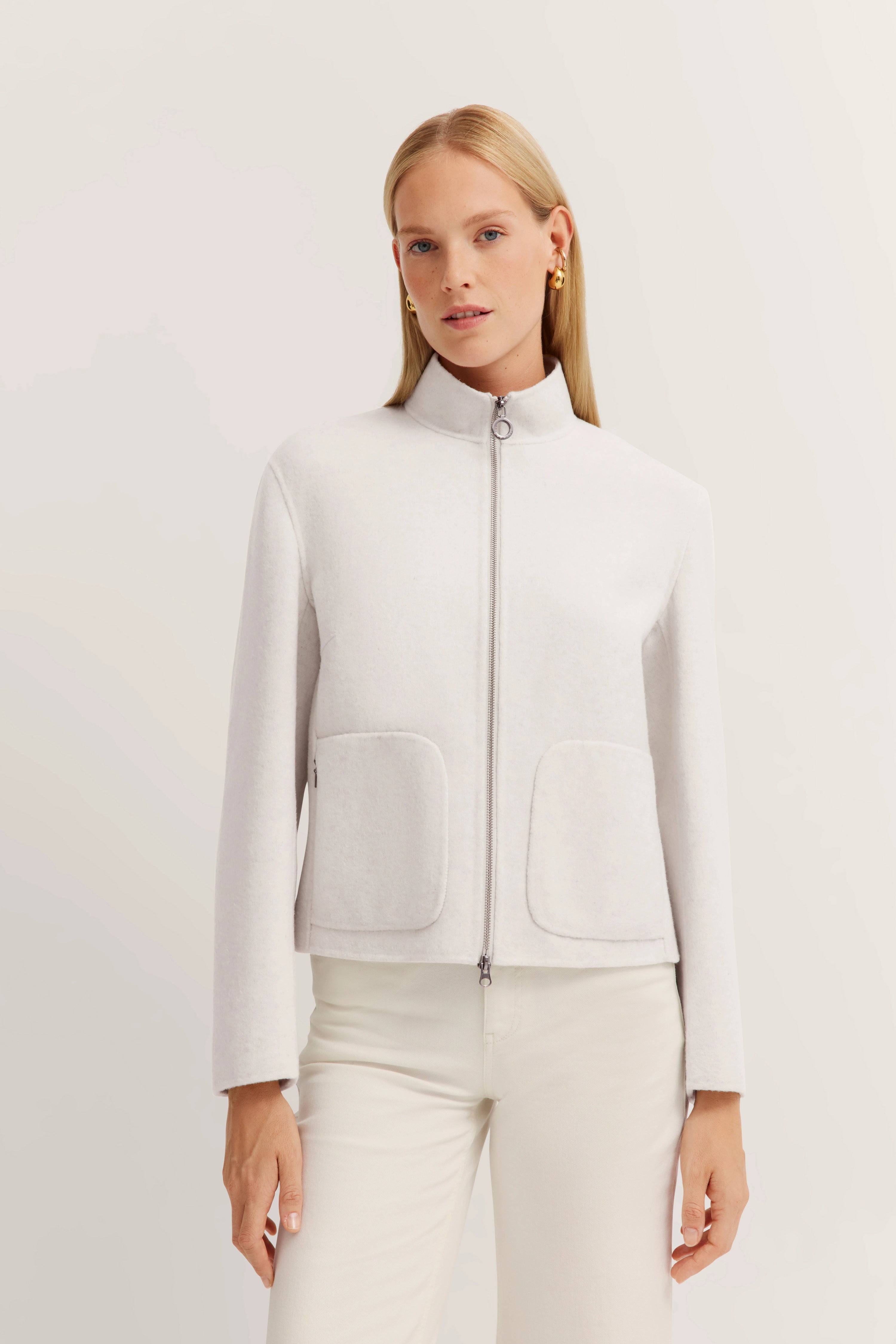 Weiße Jacke mit Reißverschluss und Taschen, getragen von Model, neutraler Blick, bugatti Stil.