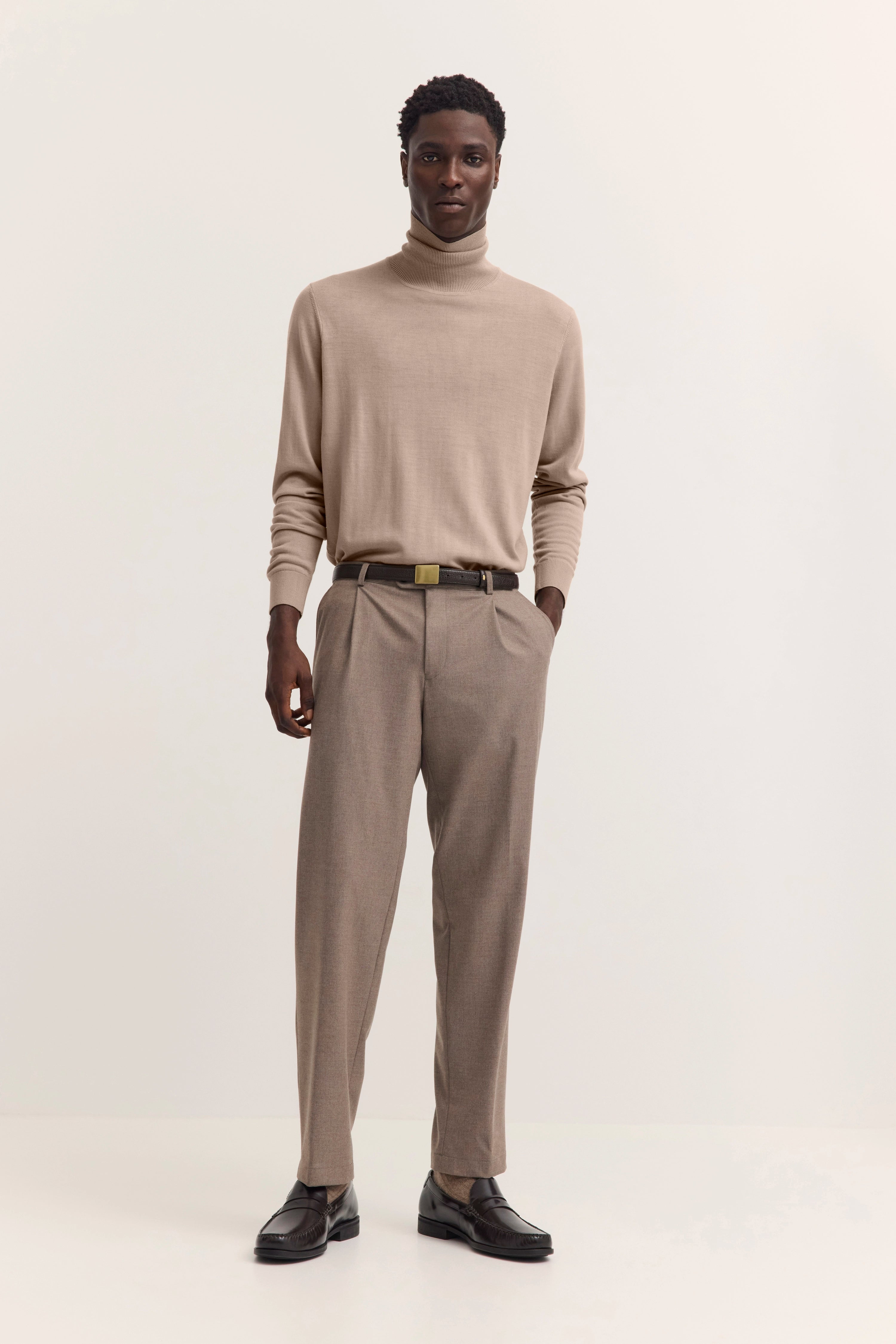 Model in beige Rollkragenpullover und Hose von bugatti, legeres Posing, elegante dunkle Schuhe.