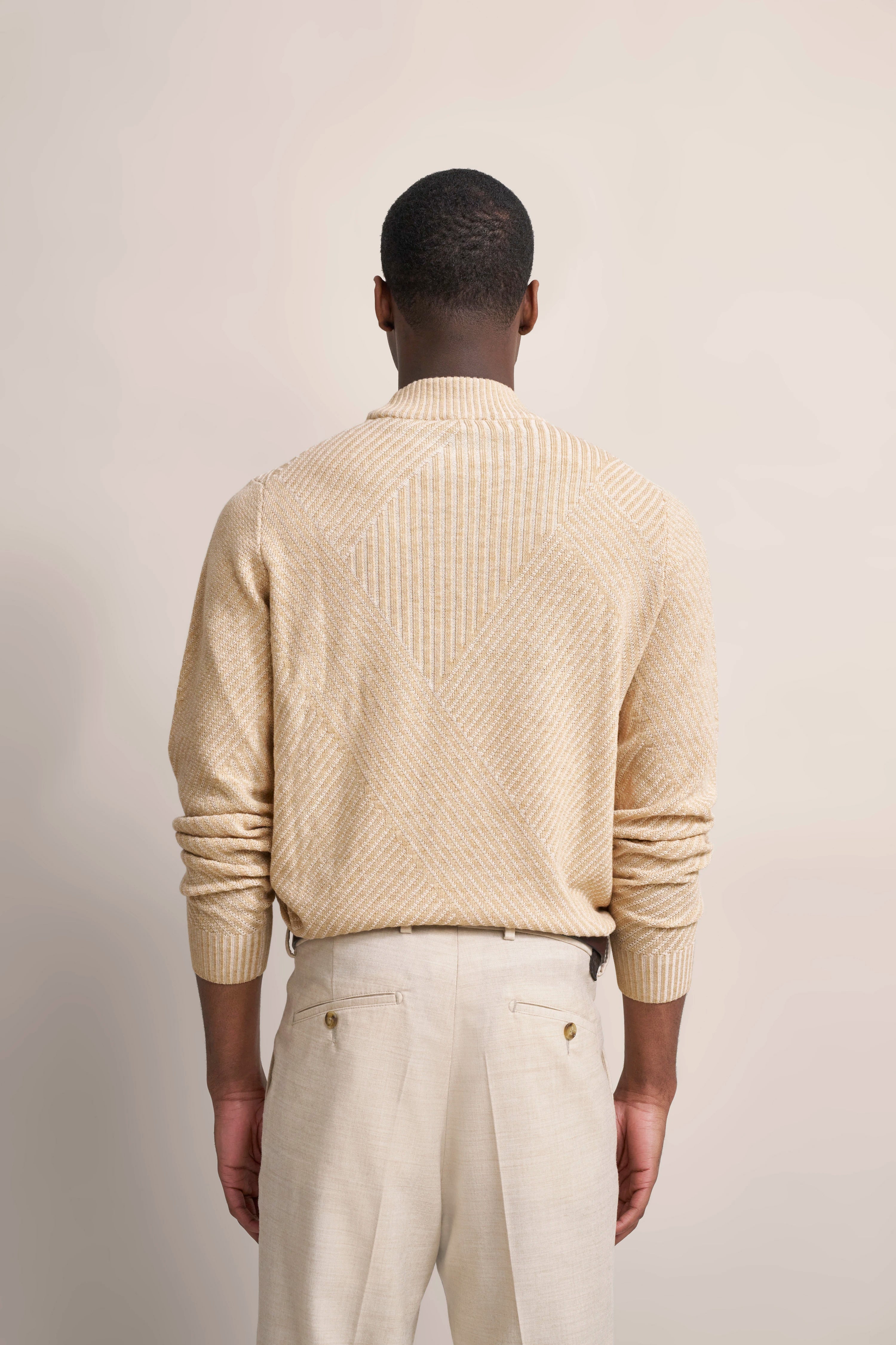 Beigefarbener Pullover mit Muster und helle Hose, Rückansicht Model, legeres Standing.