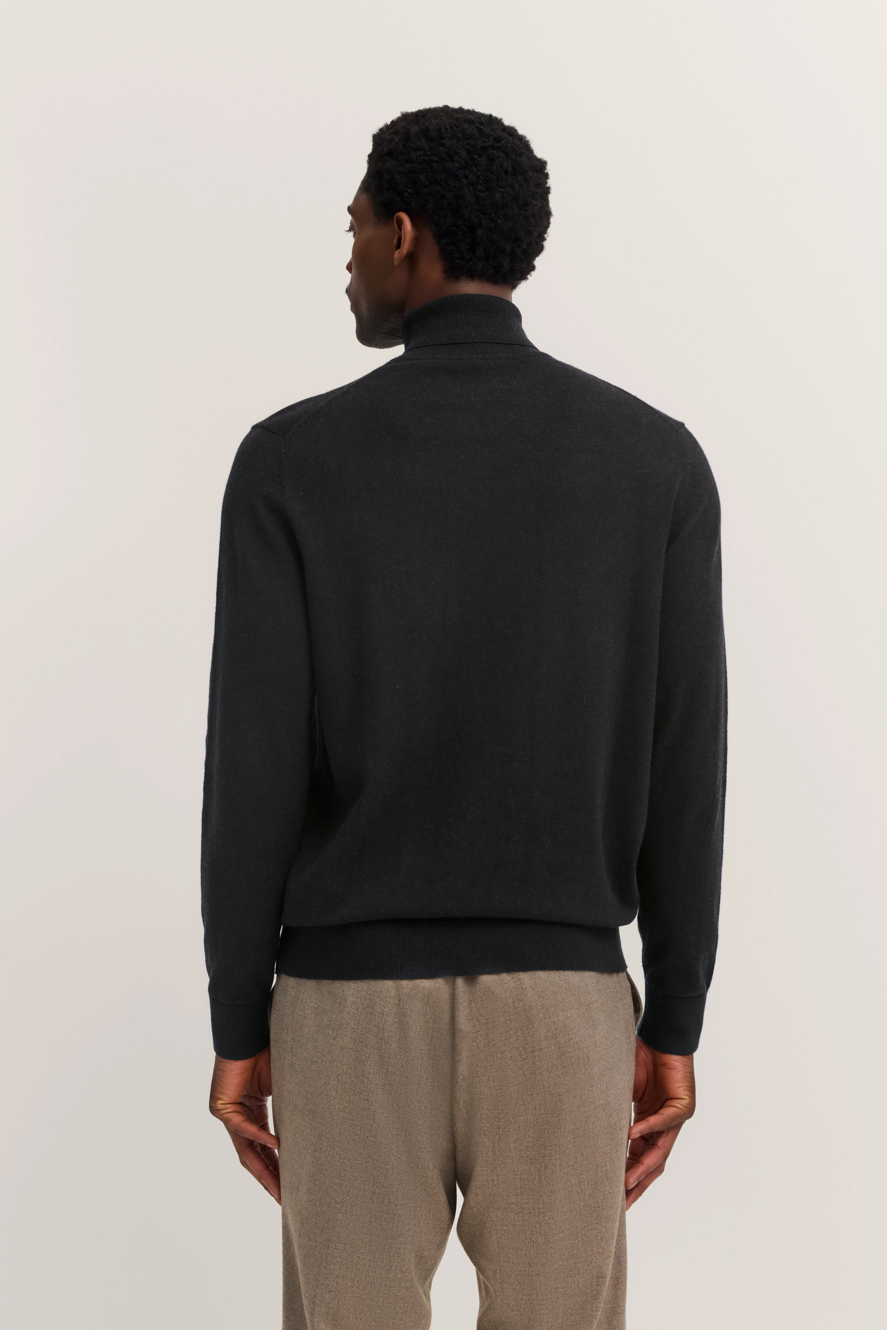 Black bugatti turtleneck sweater with beige trousers, back view, model standing relaxed.