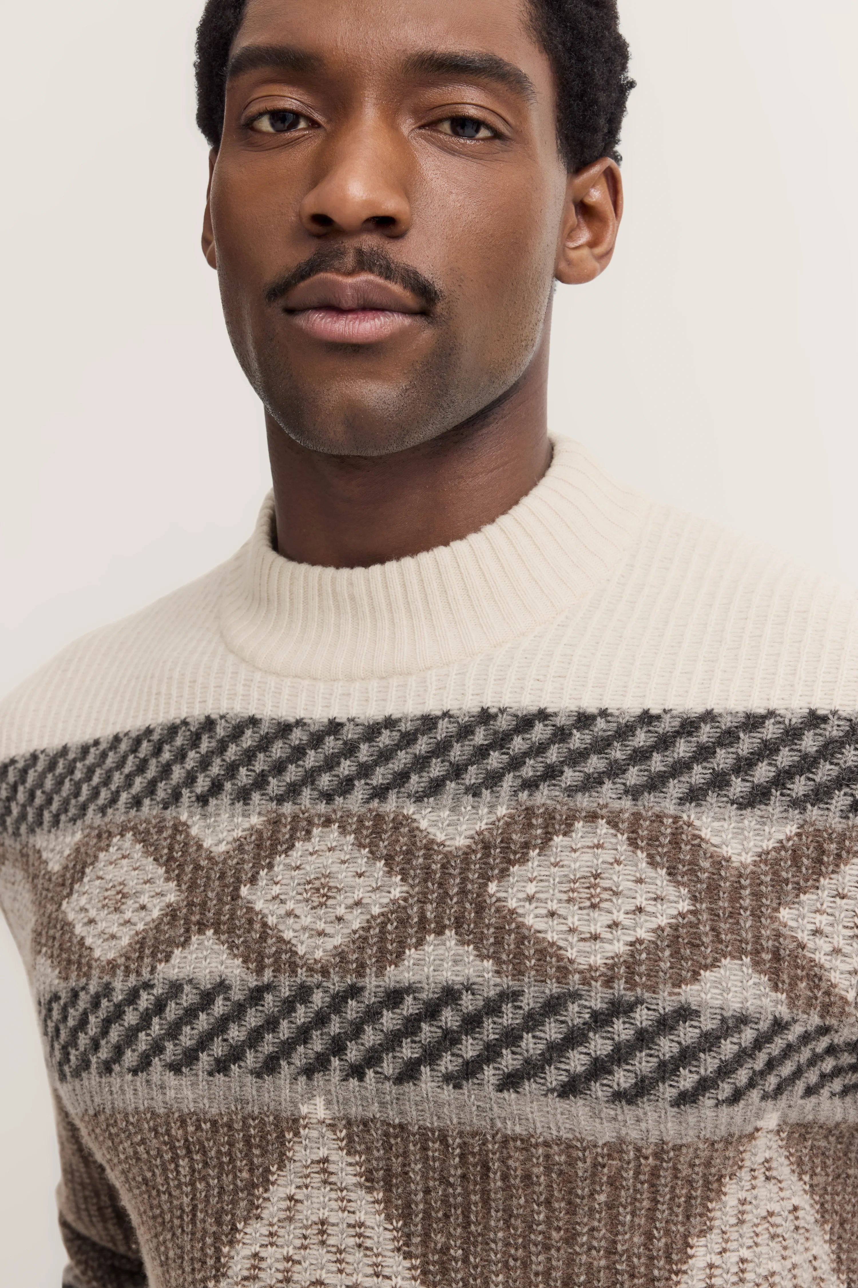 Bust of a man in a cream bugatti knit sweater with brown and gray geometric pattern.