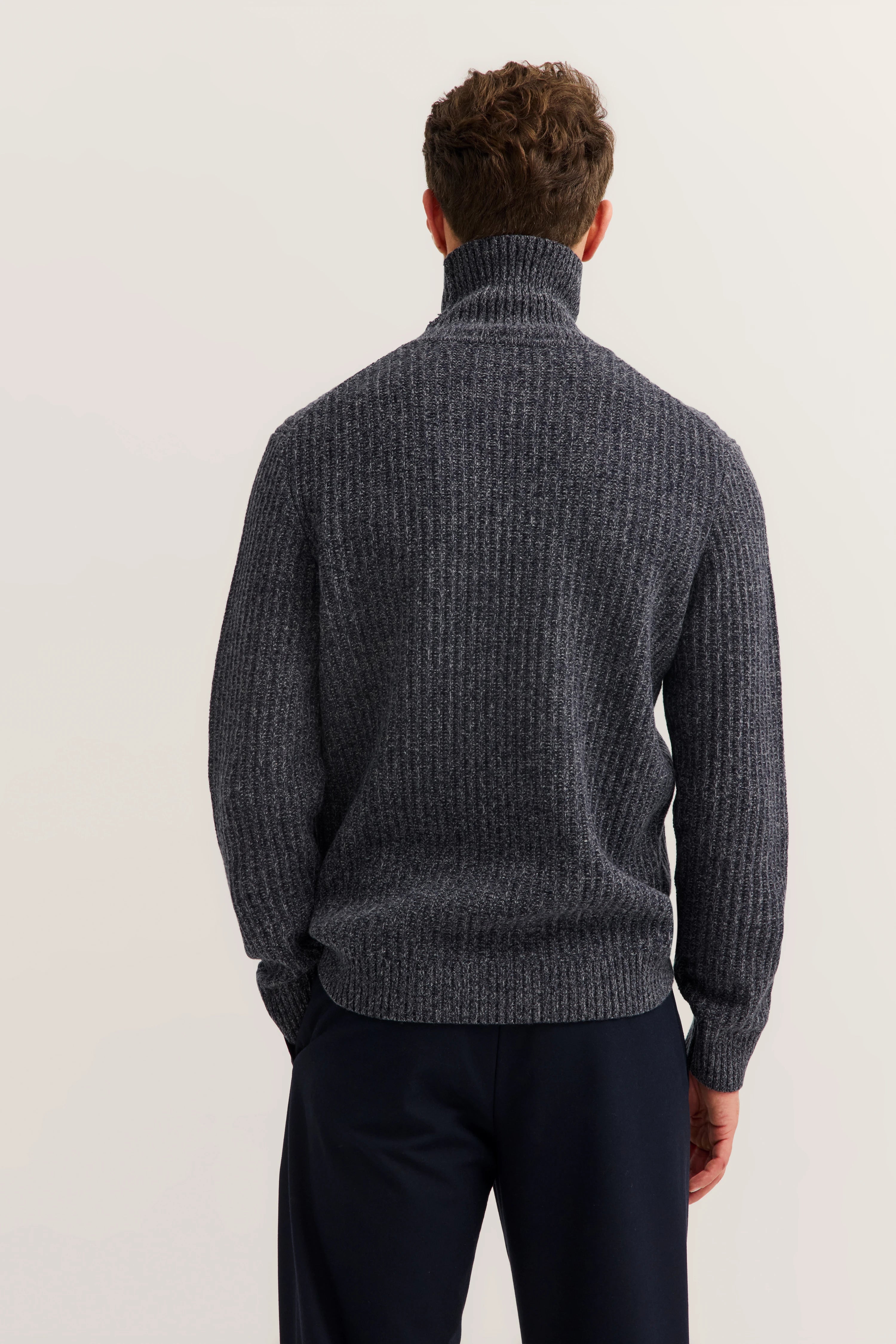 Dark grey bugatti knit sweater, back view, model stands relaxed, paired with dark pants.