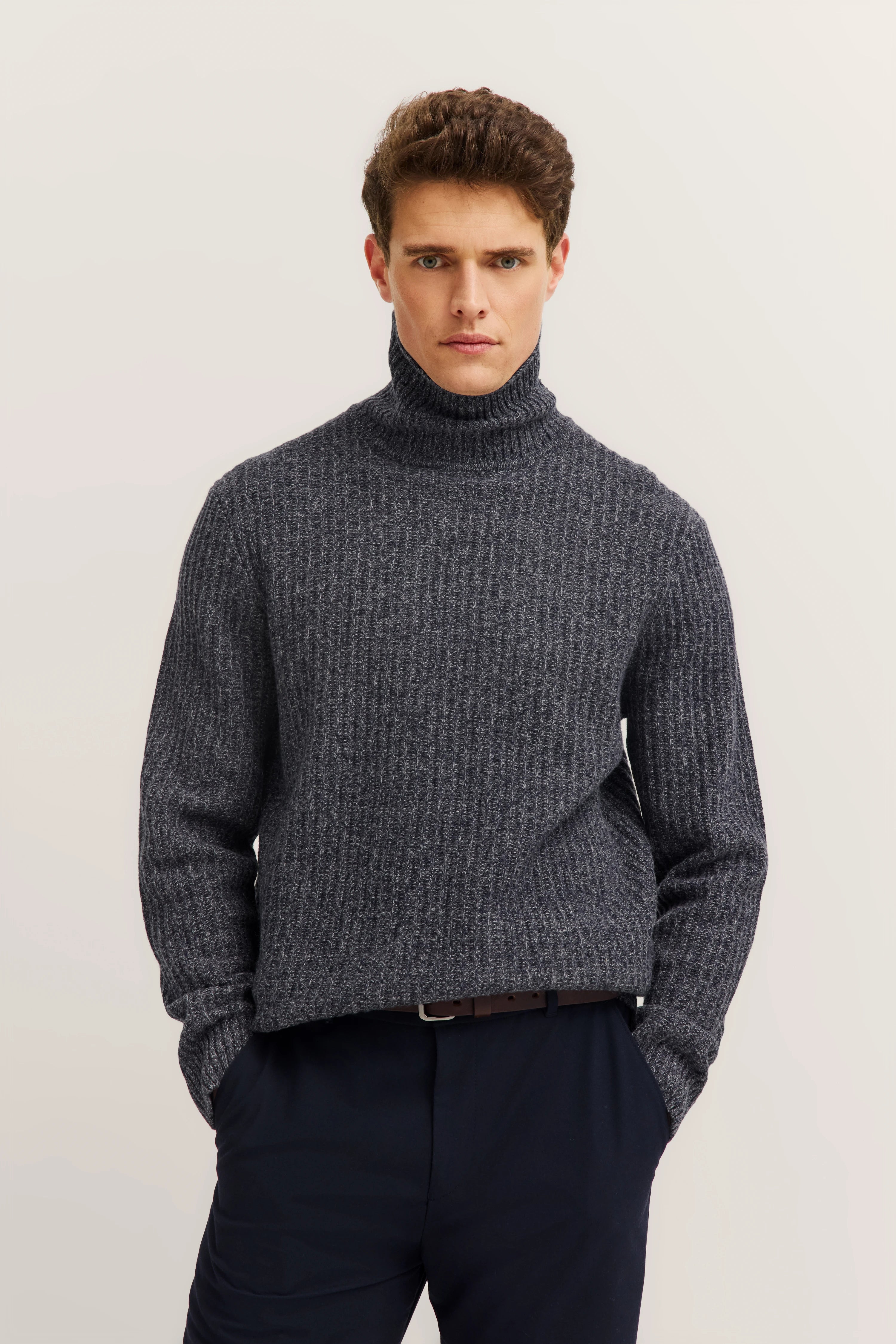 Model wearing grey bugatti turtleneck sweater, posing casually, blue pants.