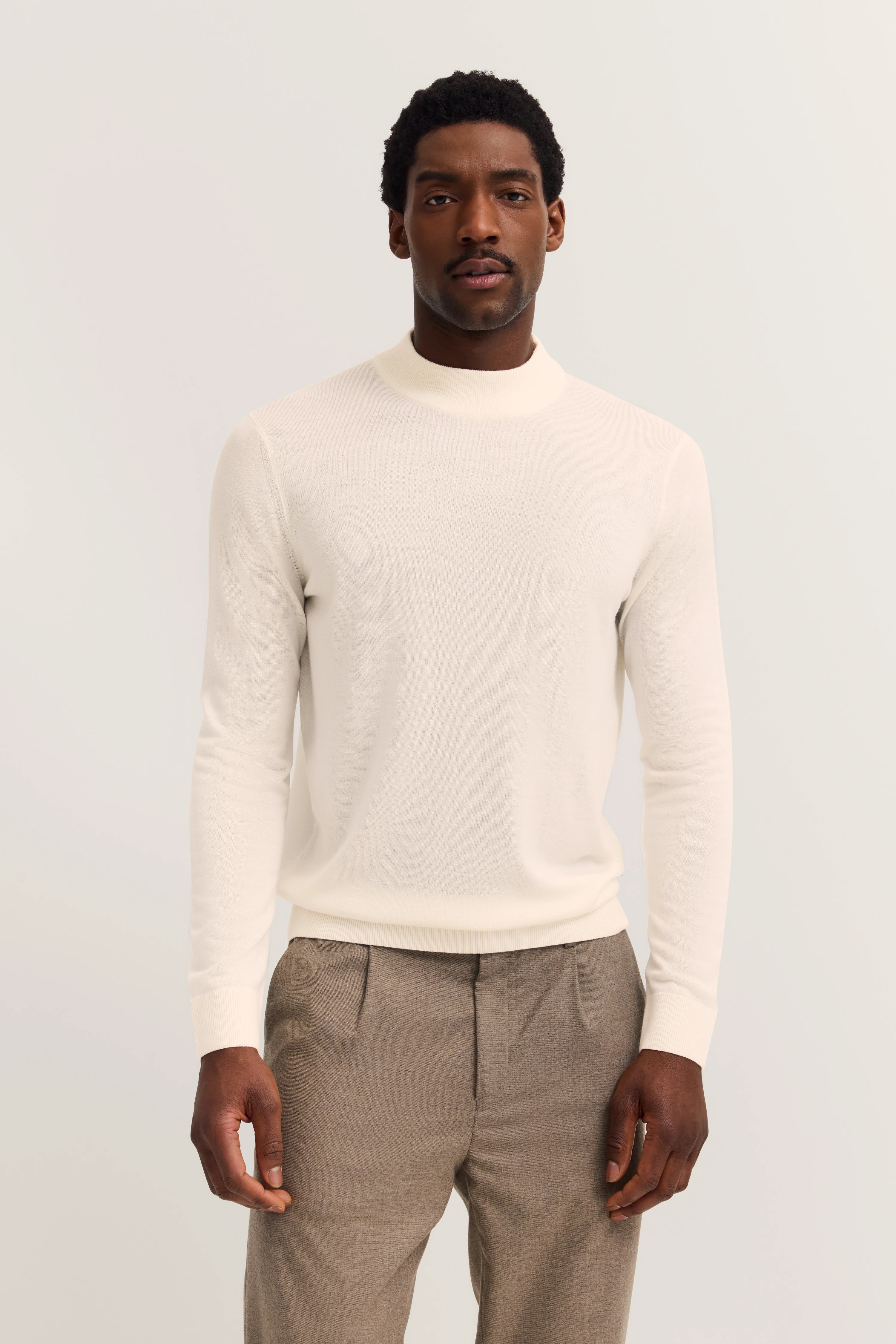 Weißer bugatti Pullover, braune Hose, Modelbild, neutraler Ausdruck.