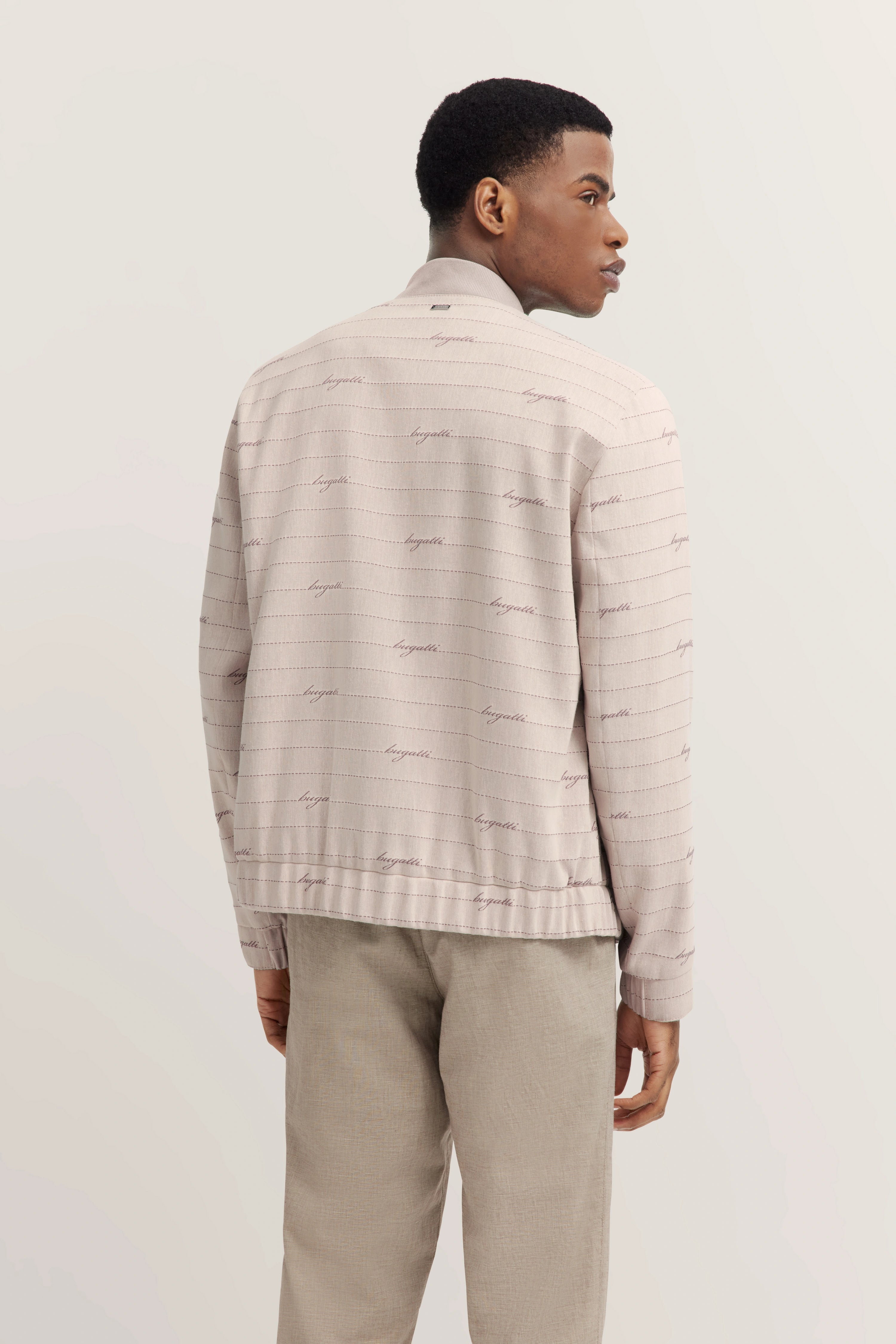 Model in bugatti beigem Jacke mit Schriftzug, locker posierend, beige Hose.