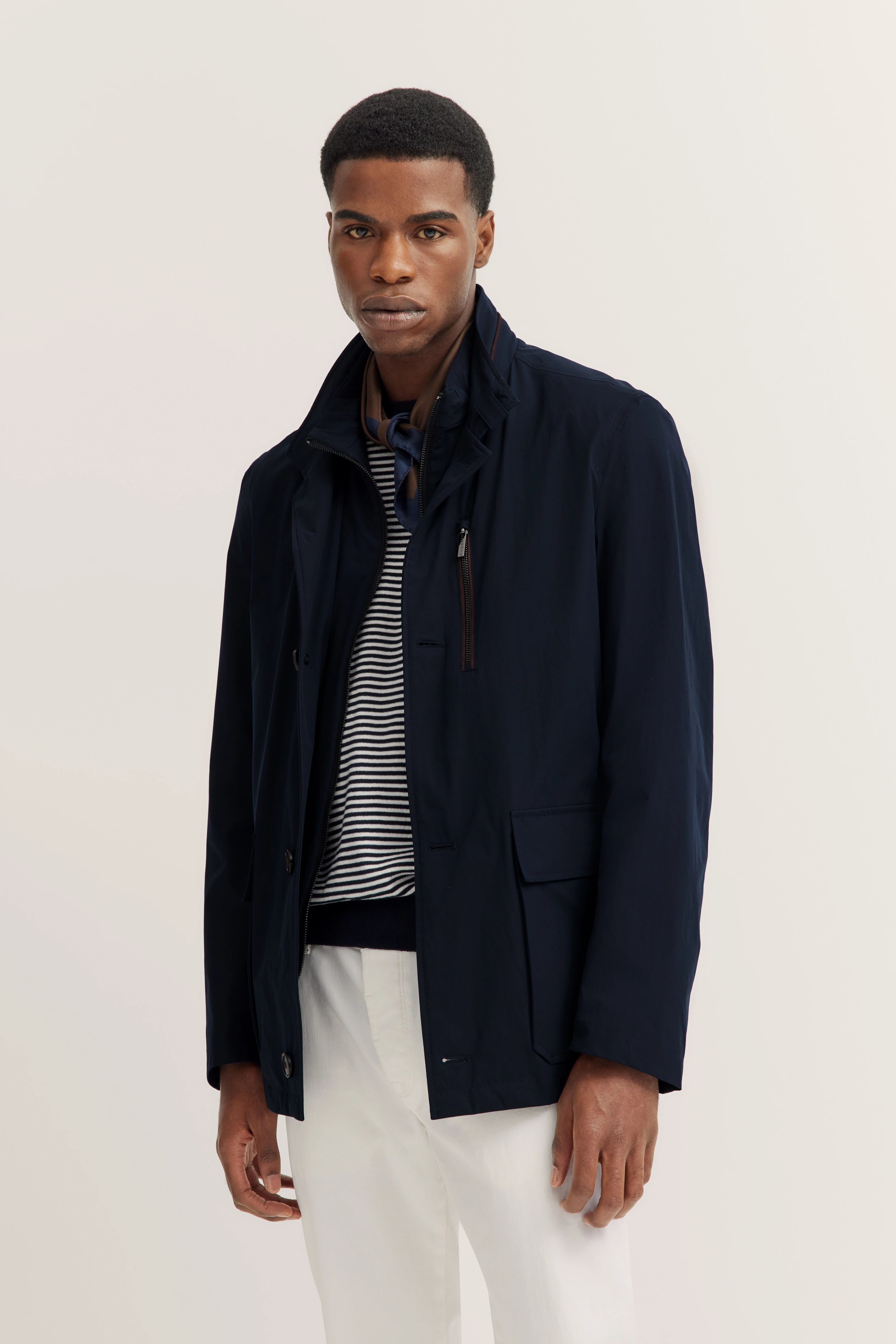 Model in navy bugatti Jacke, gestreiftes Shirt, weiße Hose, lässig entspanntes Posing.