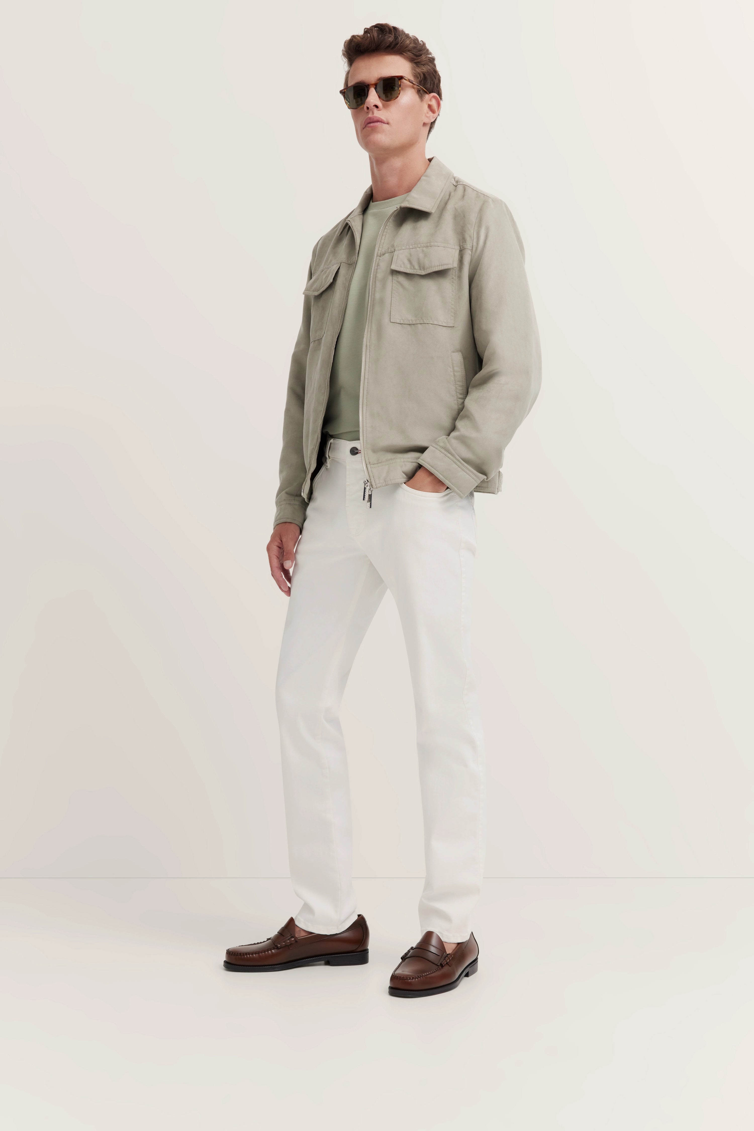 Model draagt lichtgrijze jas, groen shirt, witte broek, bruine loafers