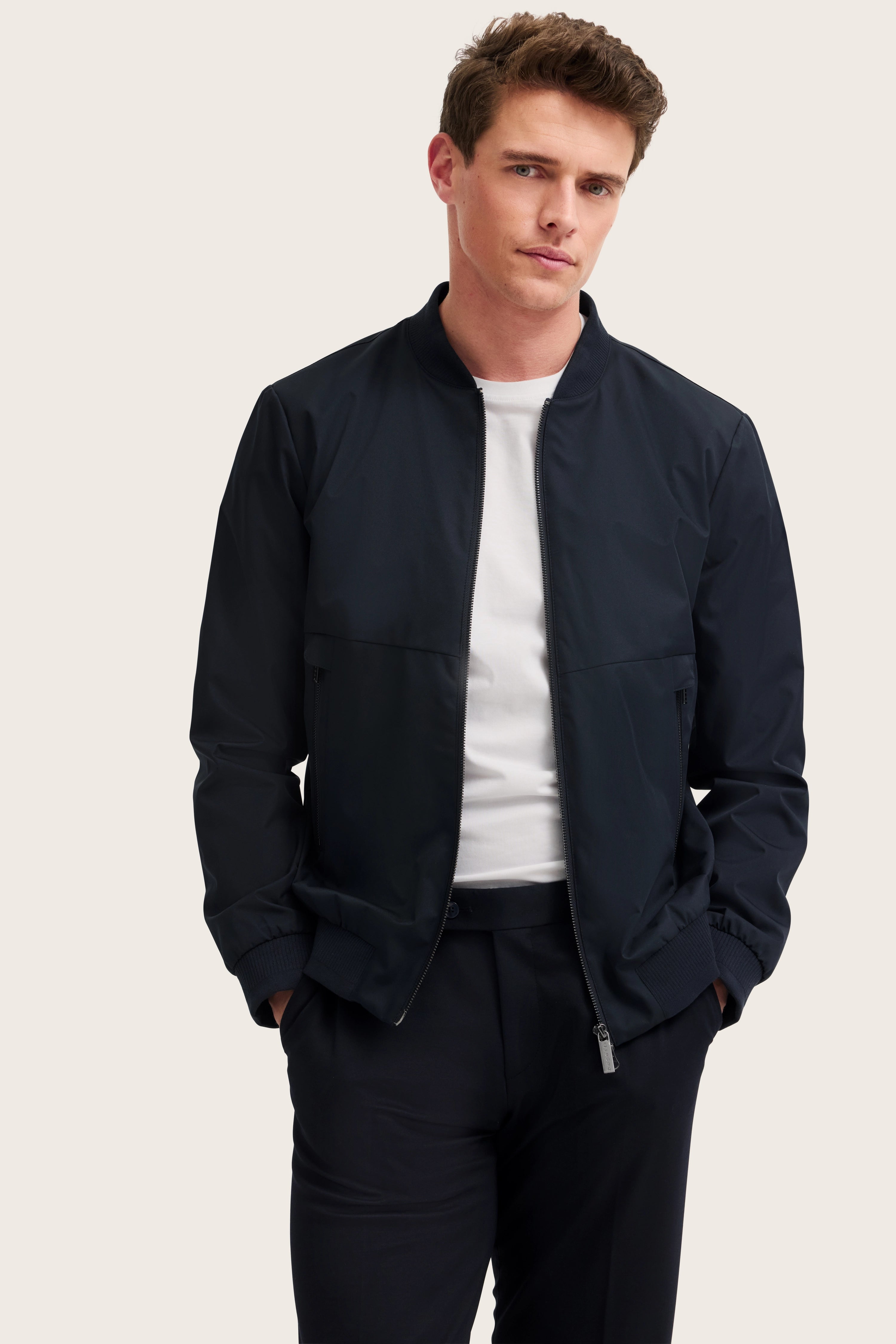 Model trägt bugatti dunkelblaue Jacke, weißes Shirt, schwarze Hose, legeres Posing.