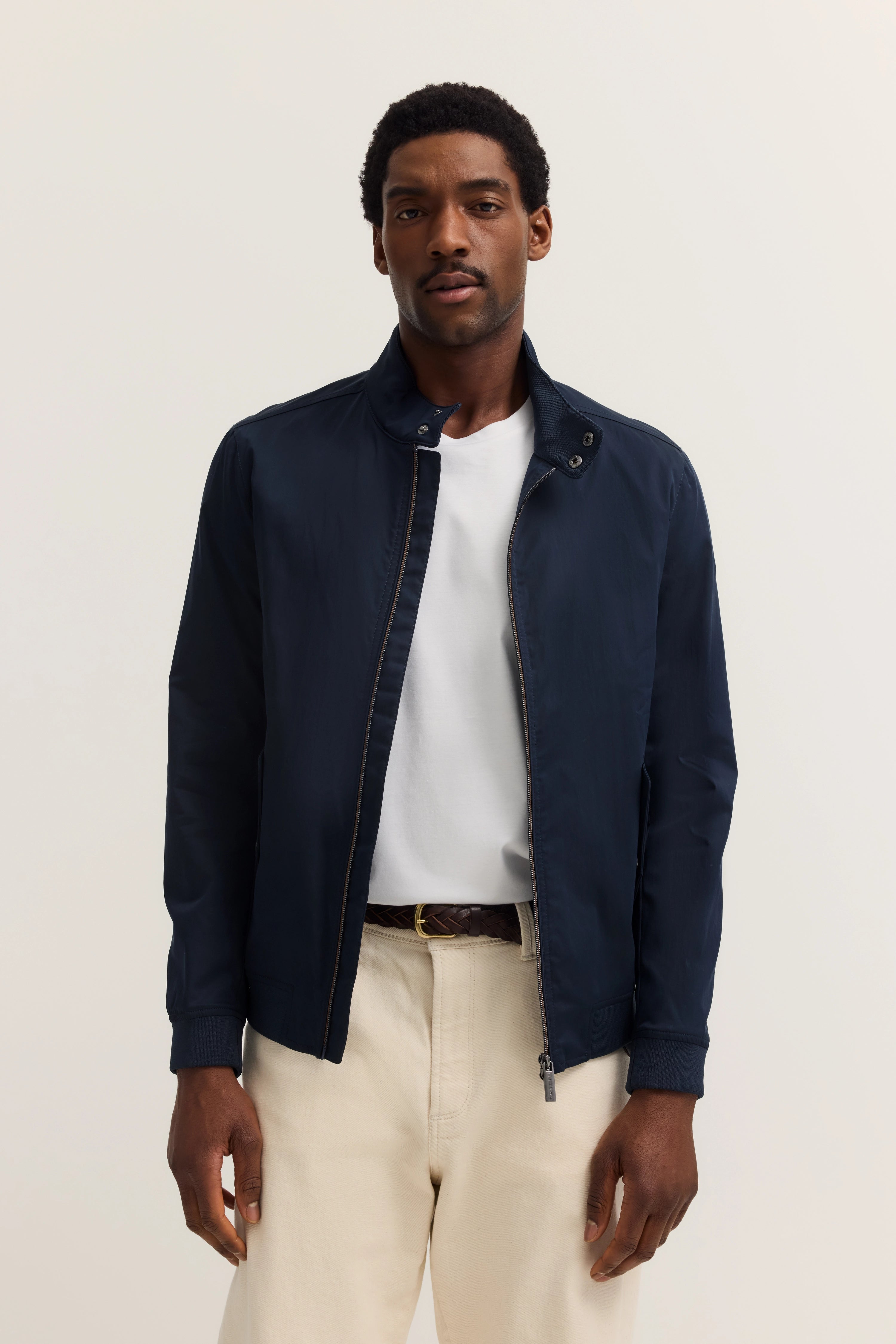 Dark blue bugatti jacket with white shirt and beige pants, model standing in relaxed pose.