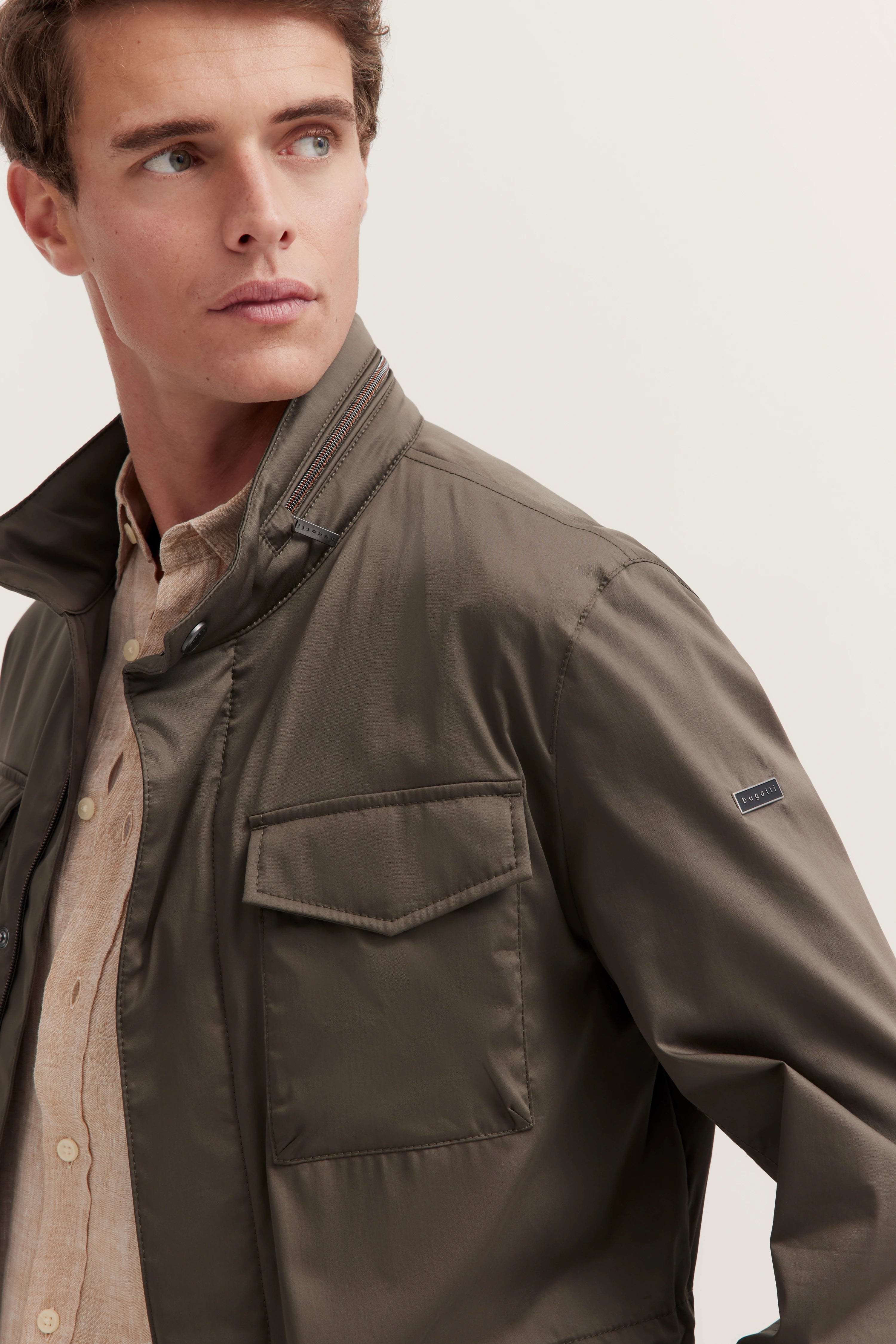 Bugatti Model in olivgrüner Jacke, beiger Hemdkragen sichtbar, elegantes Porträt, entspannter Blick.