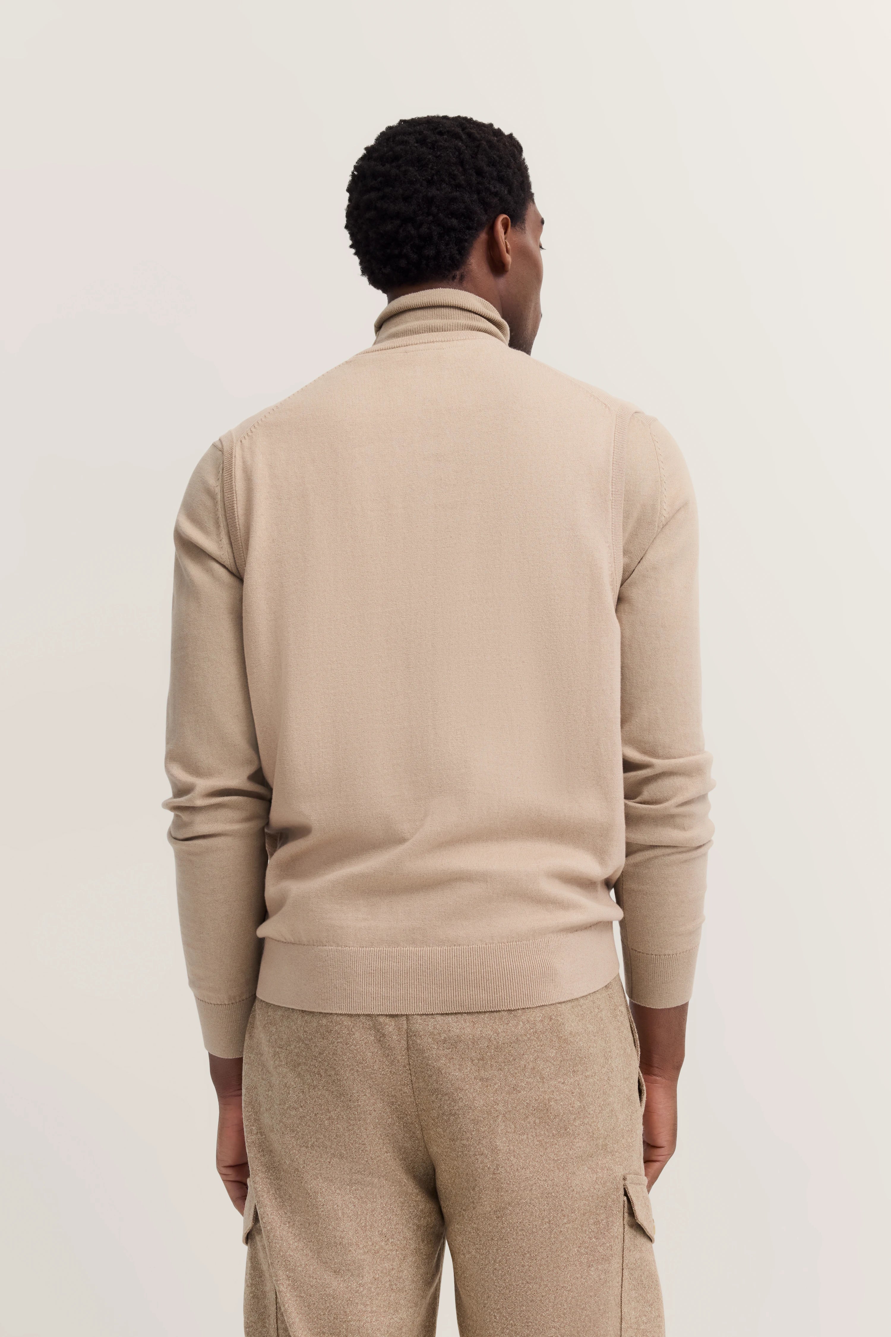 Beigefarbener Rollkragenpullover und Hose, Model von hinten.