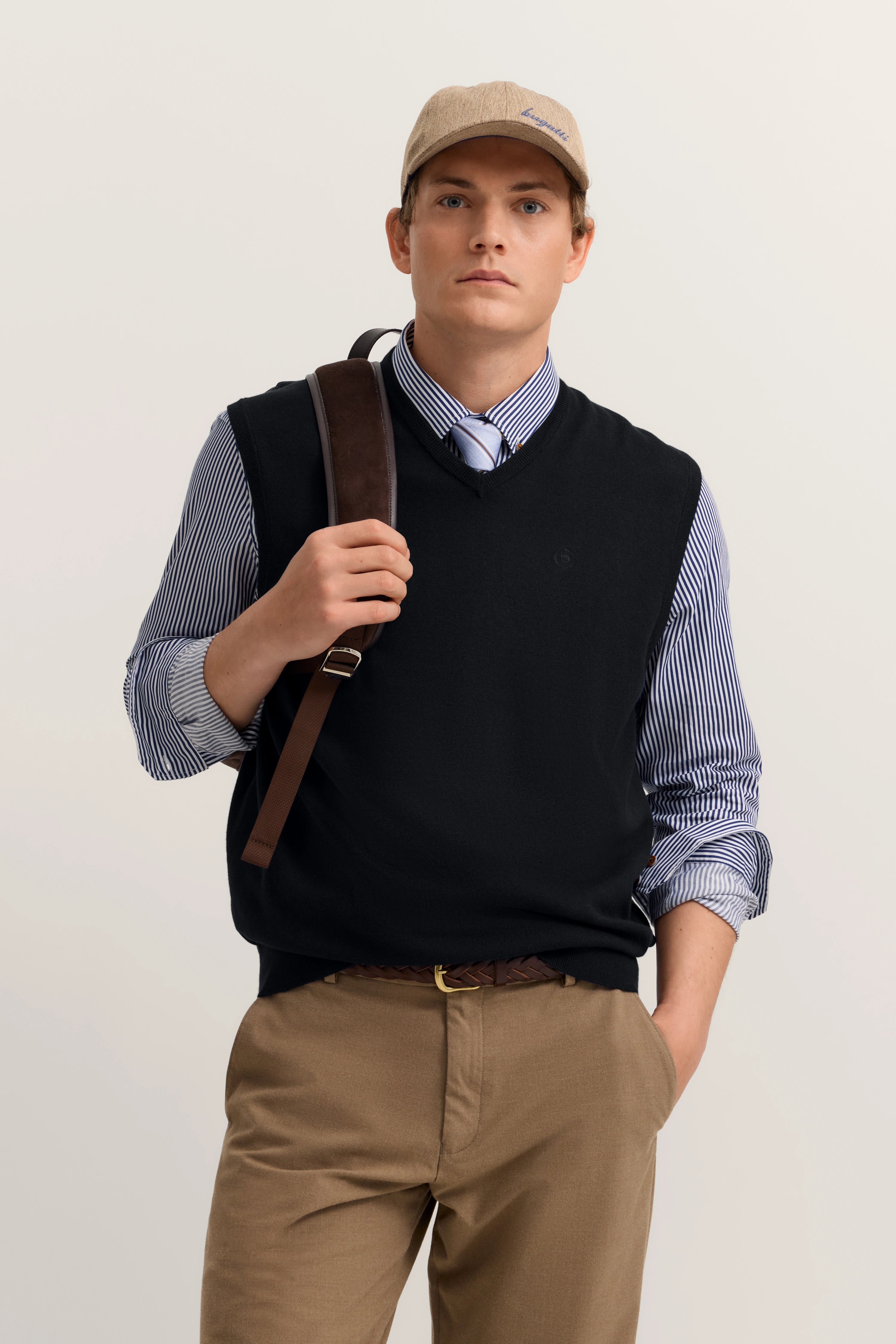 Model trägt bugatti-Basecap, gestreiftes Hemd, schwarze Weste, braune Hose. Lässig mit Rucksack.