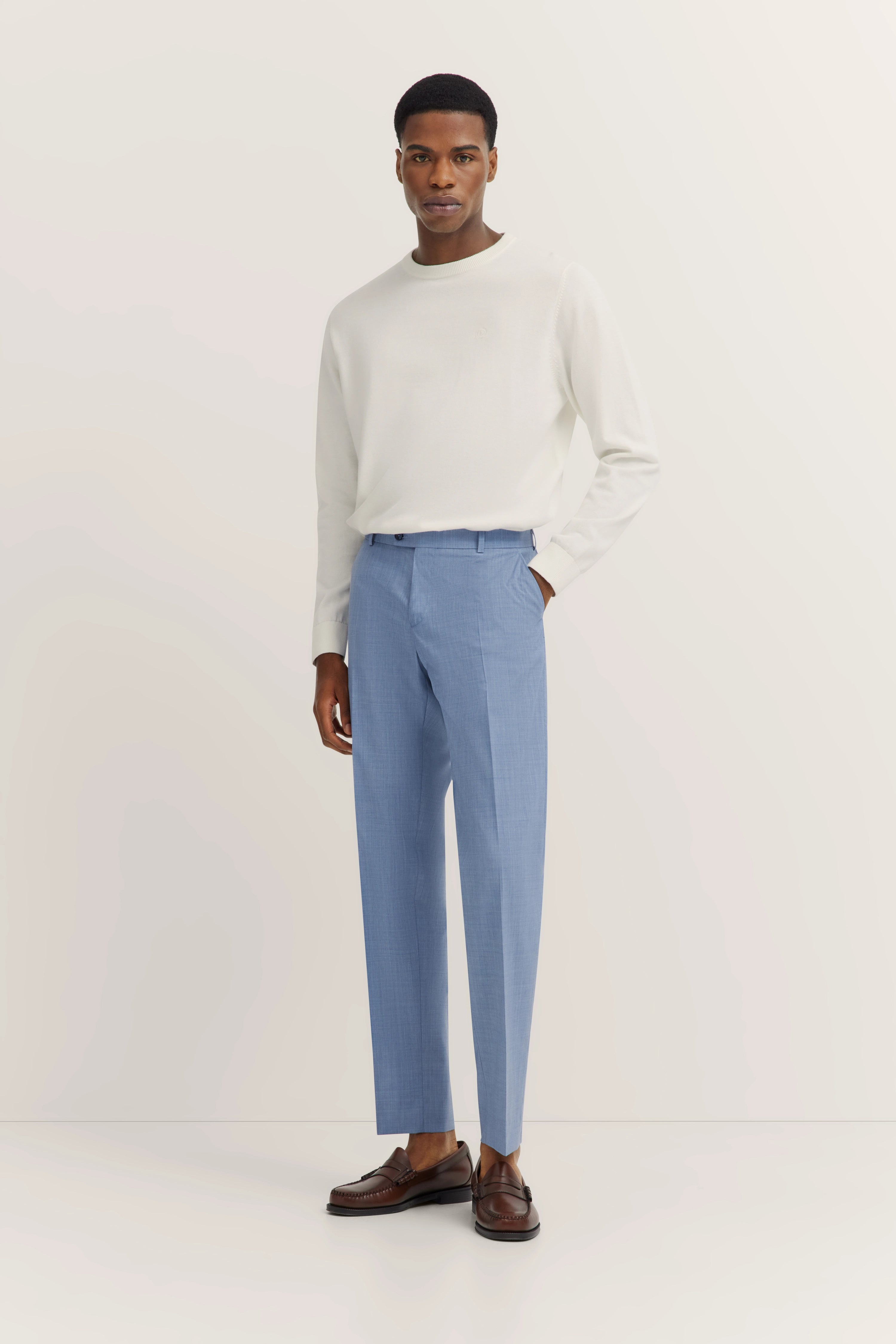 Achteraanzicht van model in blauwe bugatti broek en witte trui, klassieke bruine schoenen.