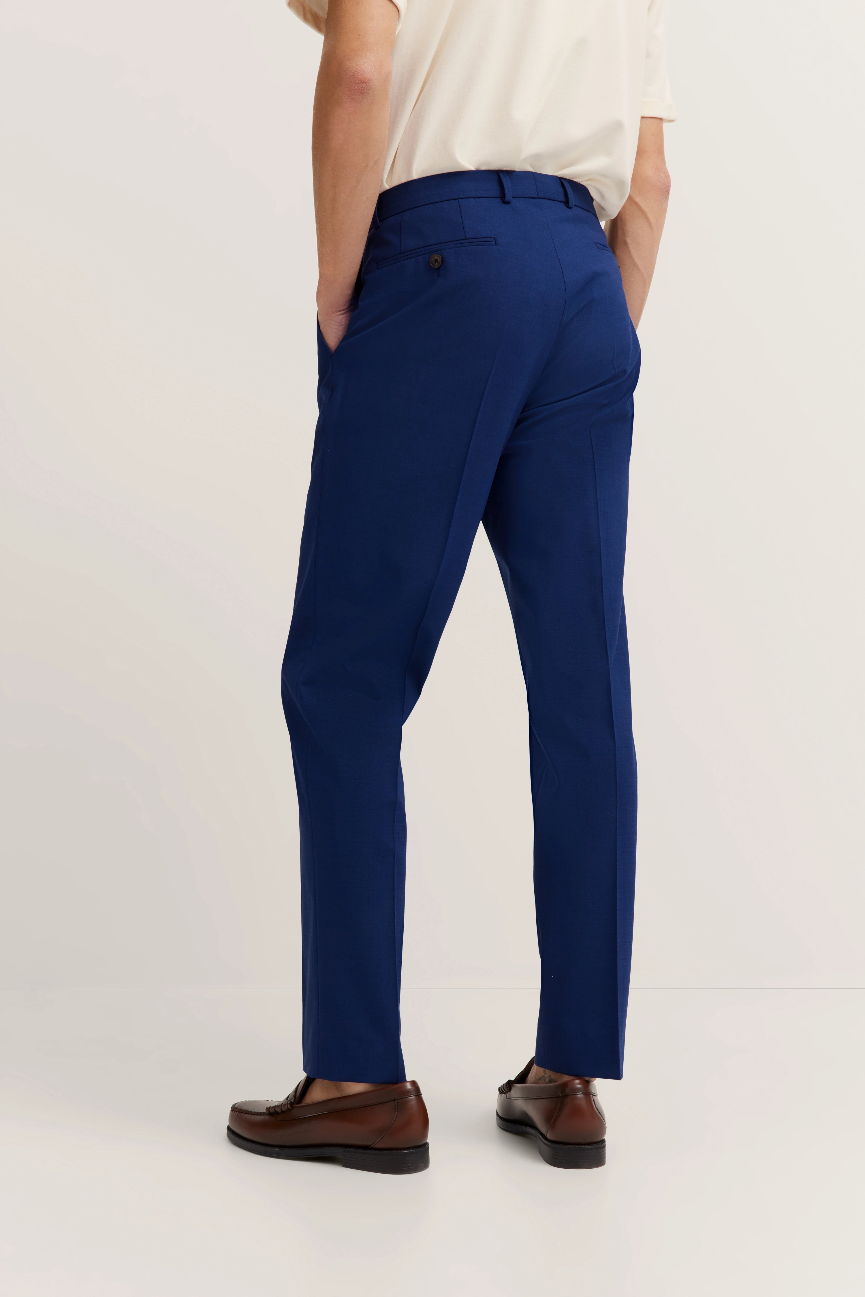 Blaues bugatti-Modellfoto, beige Hemd, braune Schuhe, legeres Posing, Hände in Hosentaschen.