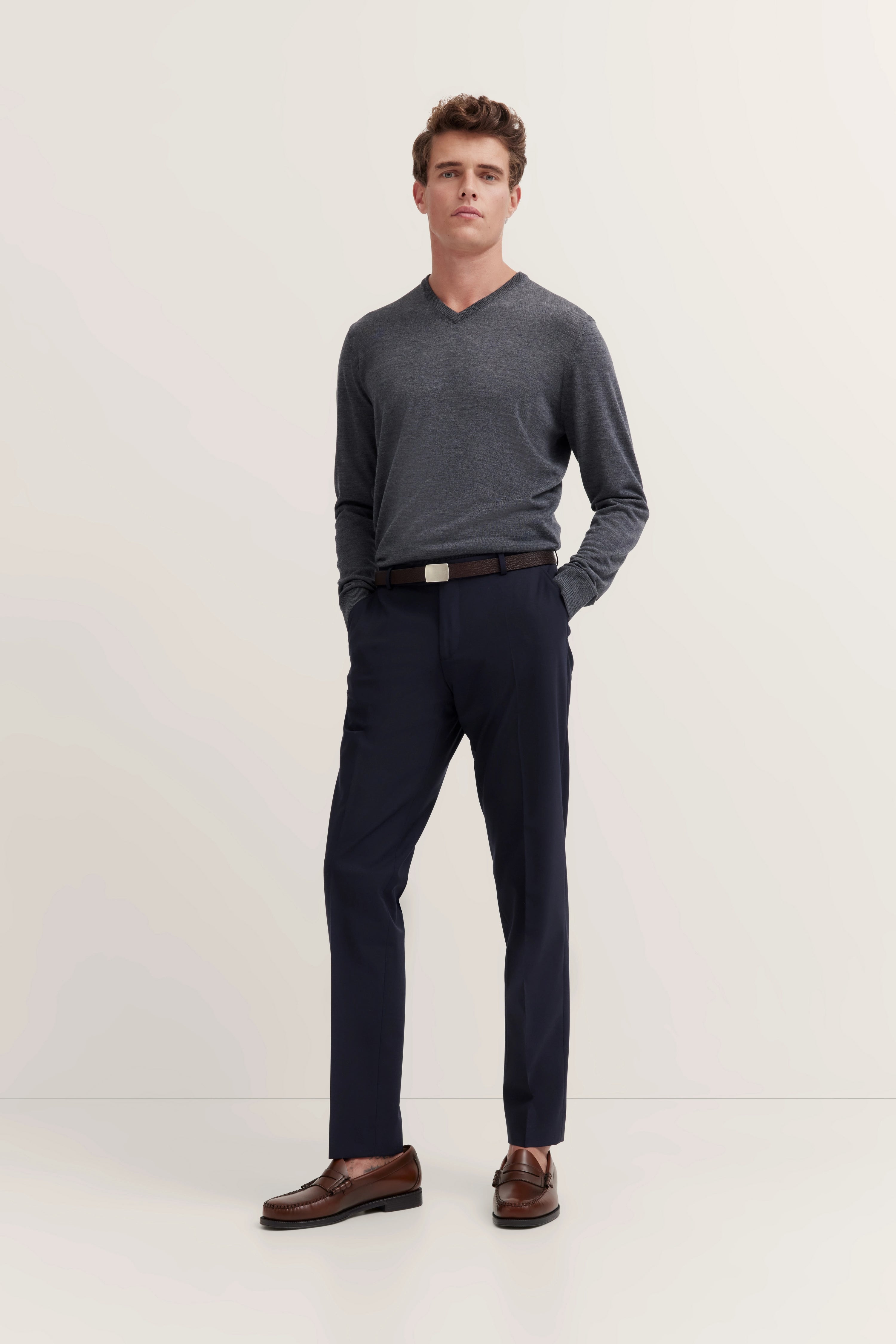 bugatti Outfit: Grauer Pullover, dunkelblaue Hose, braune Schuhe, modelhaftes Stehpose, Rückansicht.
