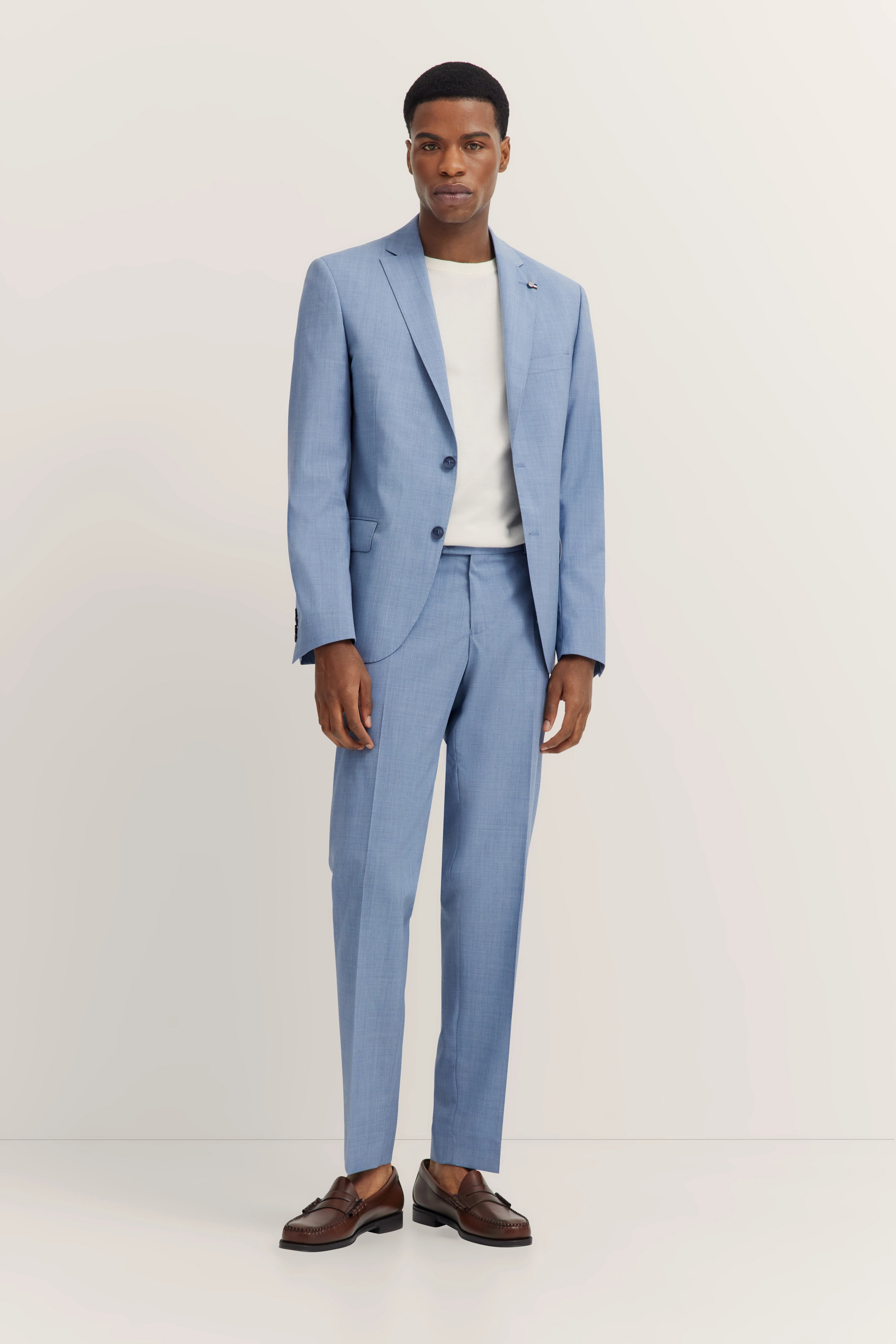 Model in lichtblauw bugatti-pak, wit shirt, bruine loafers, ontspannen houding.