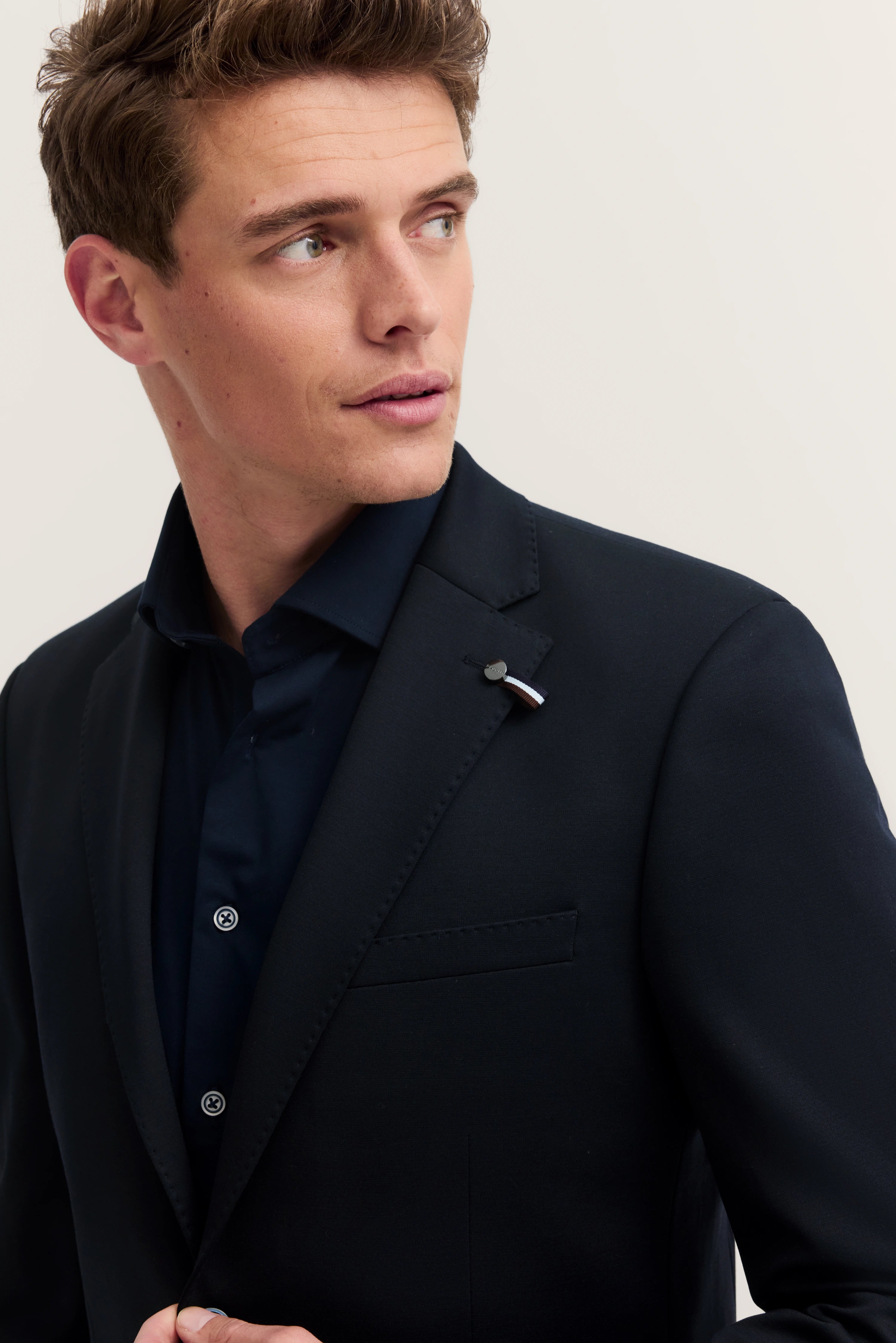 Alt-Text: Elegantes Modelbild: Mann im schwarzen bugatti Anzug mit dunkelblauem Hemd, Blick zur Seite.