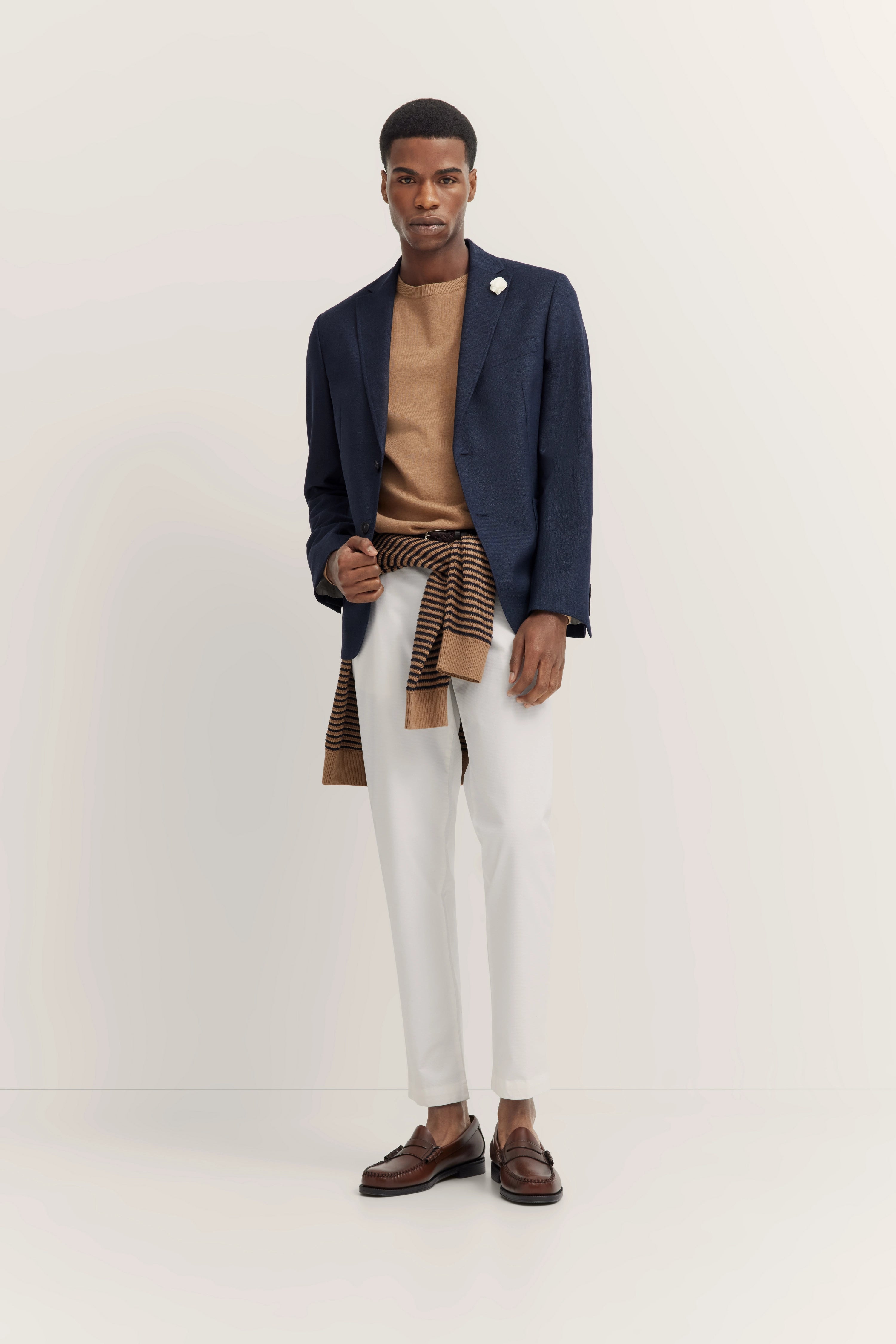 Elegant model in marineblauw colbert, beige trui, witte broek en bruine schoenen van bugatti.