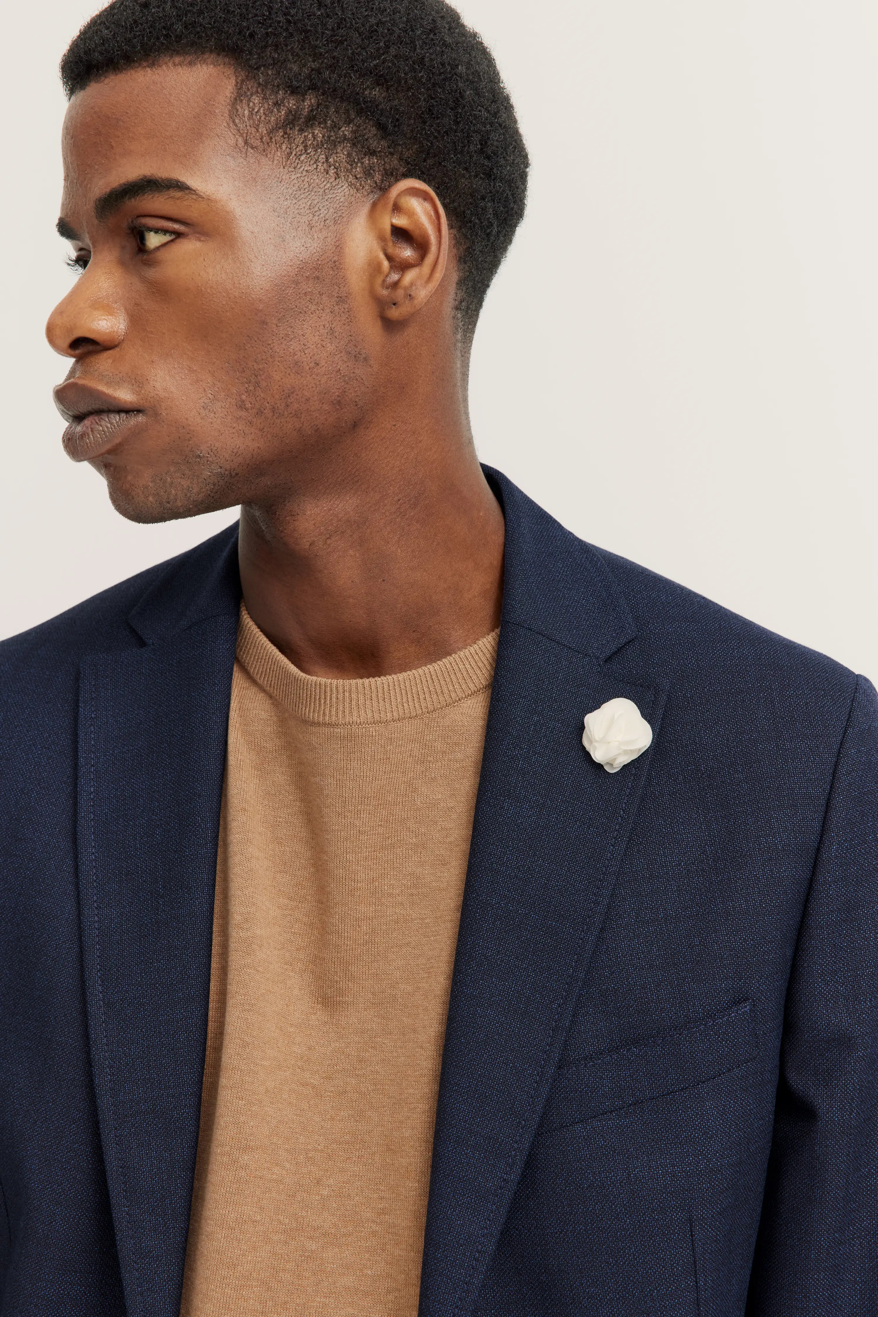 Bugatti Model mit blauem Sakko und beigem Pullover, Seitenprofil, stilvoll und elegant.
