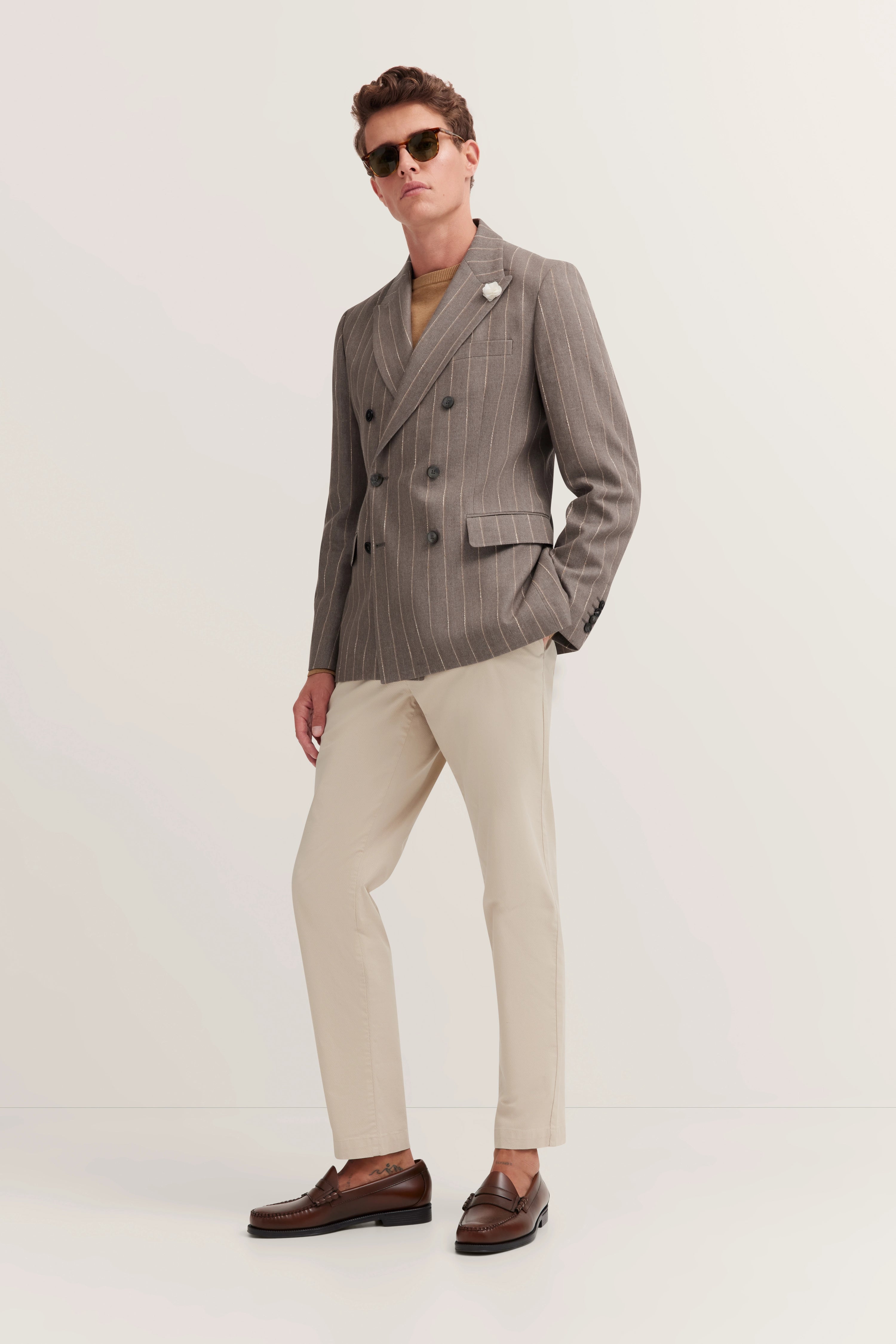 Grauer Nadelstreifenanzug, beige Hose, braune Loafers, Model steht lässig, eleganter Look von bugatti.