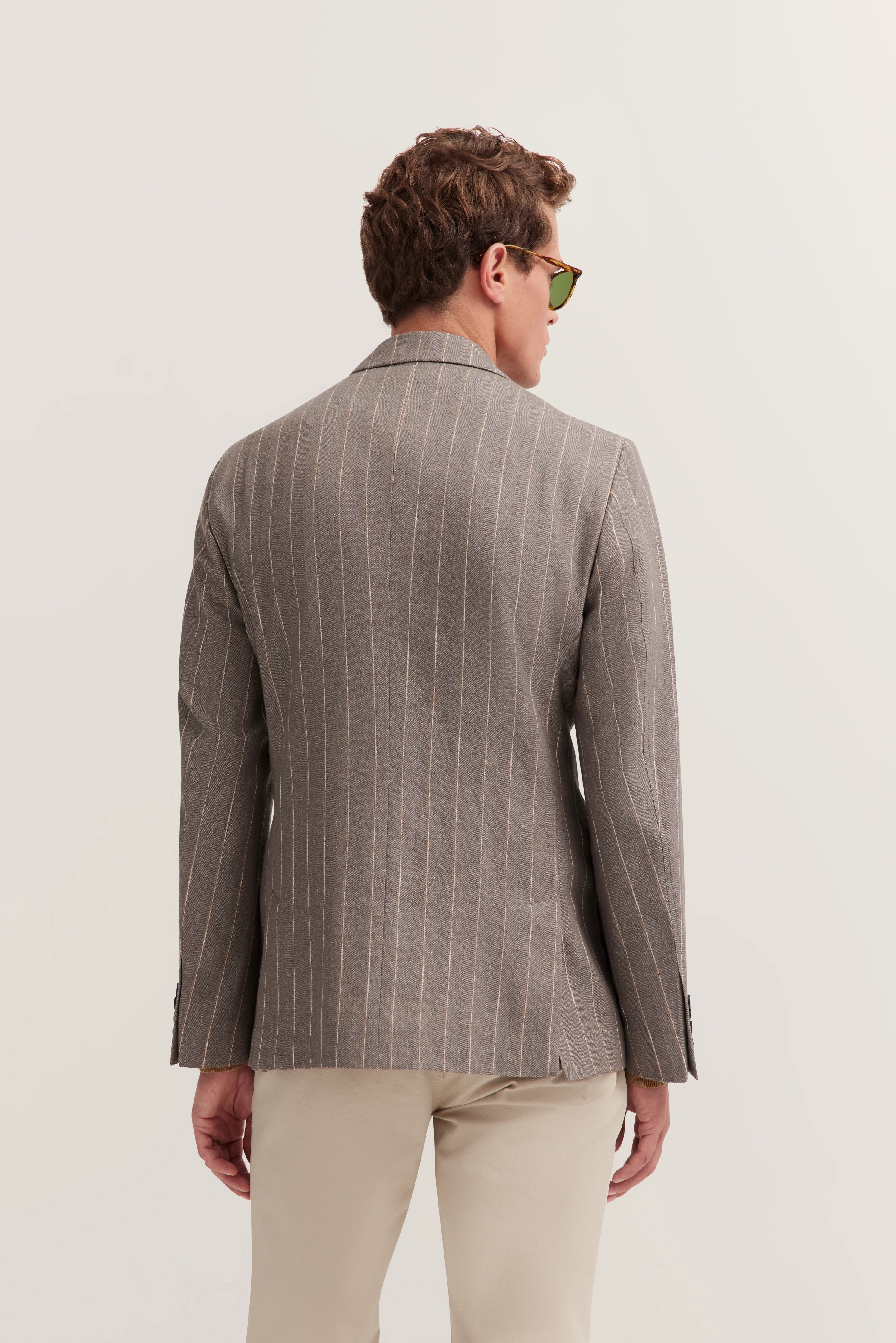 Grauer Nadelstreifen-Blazer, Rückansicht, getragen von Model mit Sonnenbrille, beige Hose.