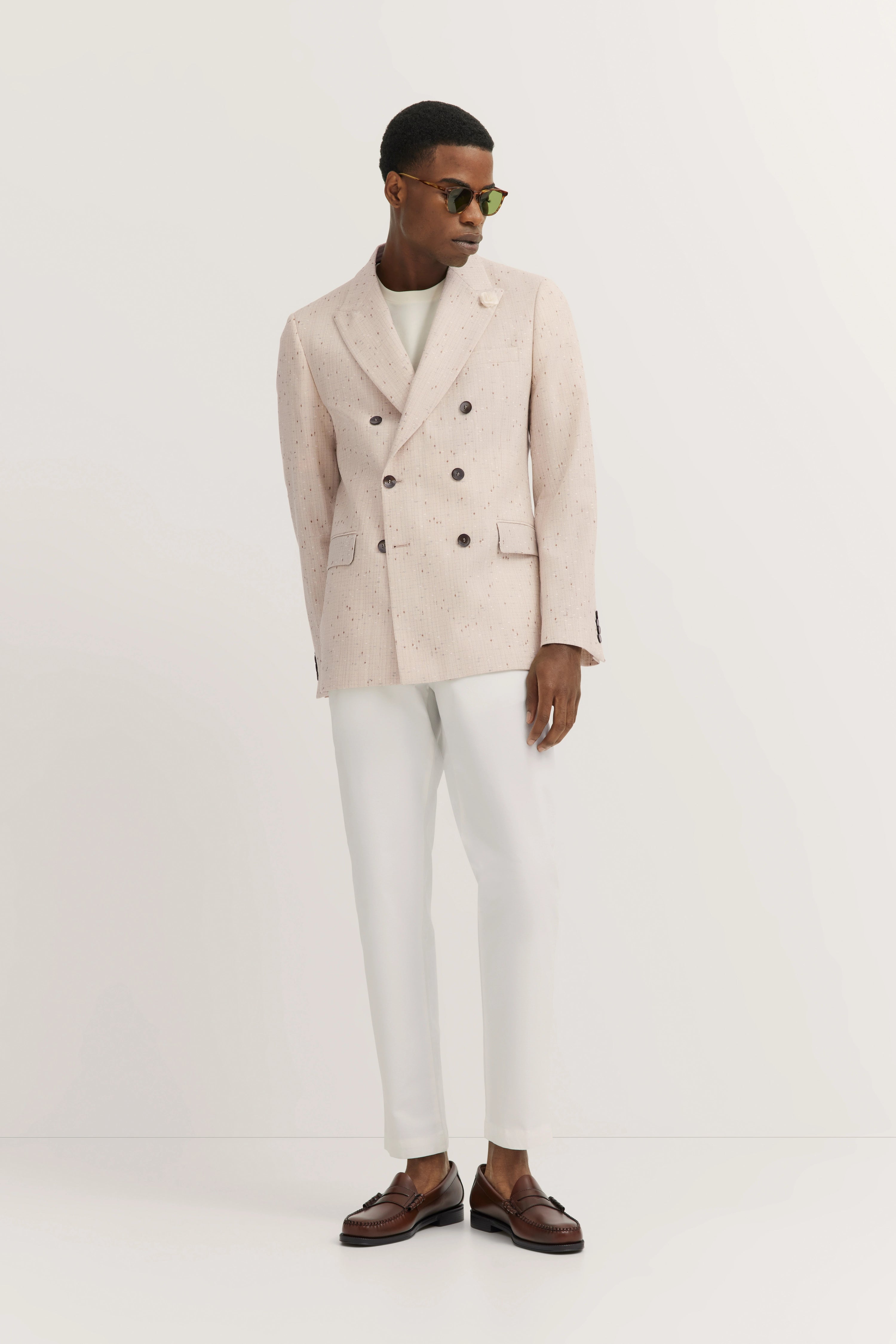 Elegante model in beige bugatti double-breasted blazer, witte broek, bruine loafers, zijwaarts blik.