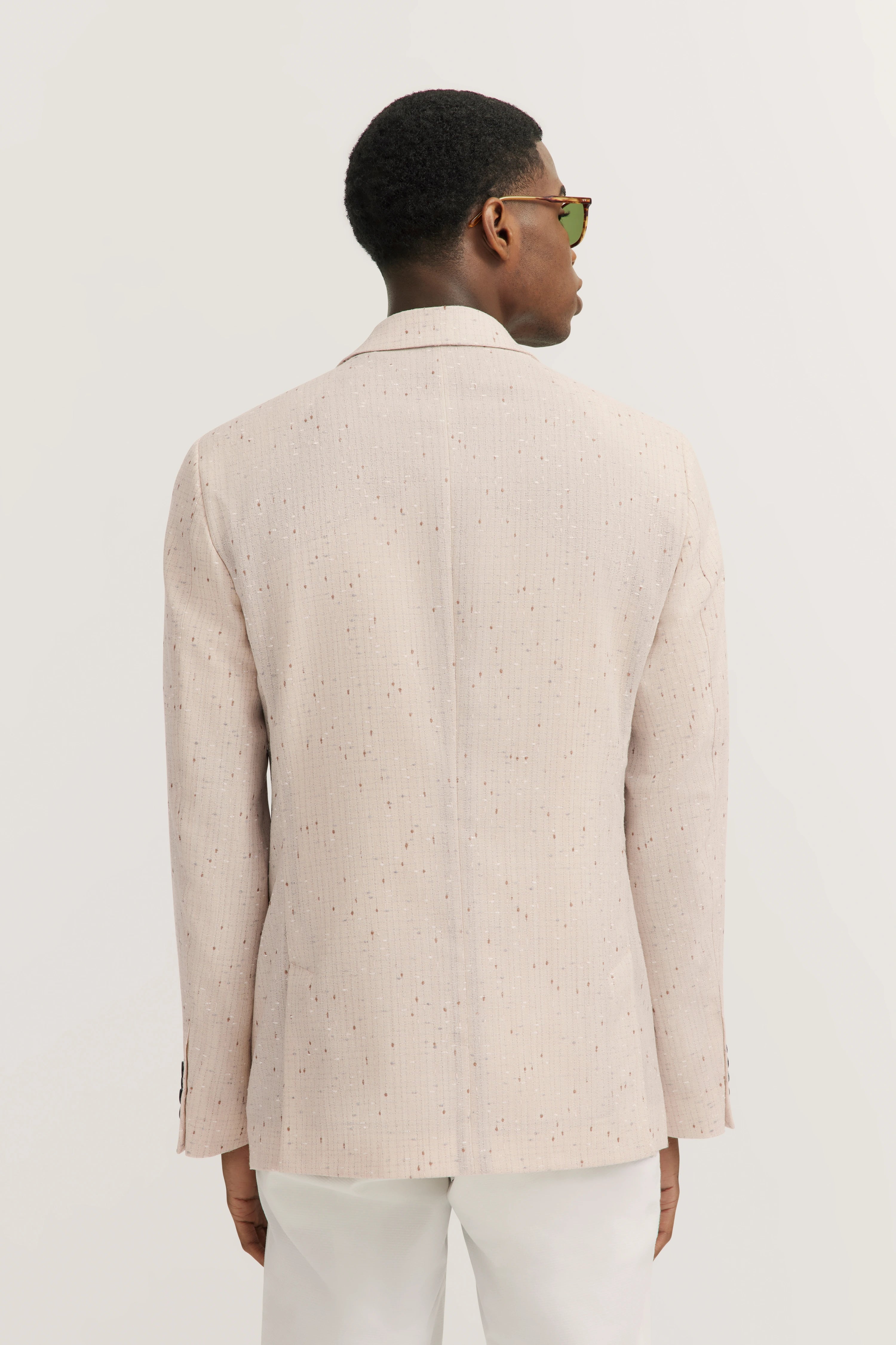 Beige bugatti colbert met subtiel patroon, model van achteren, ontspannen houding.