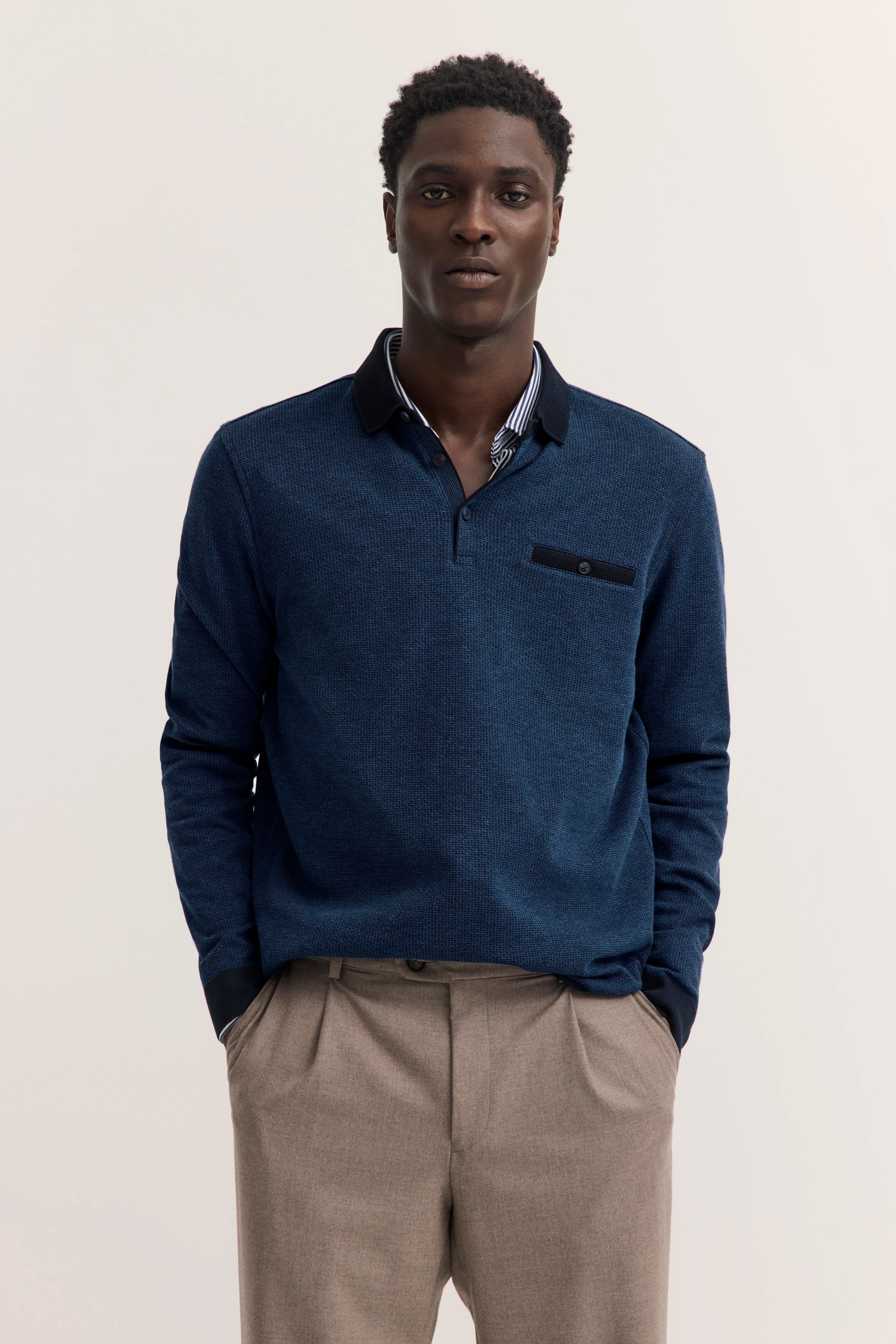 Bugatti Model in blauem Pullover und beigen Hosen, legeres Posing, Stil und Geschmackssicherheit.